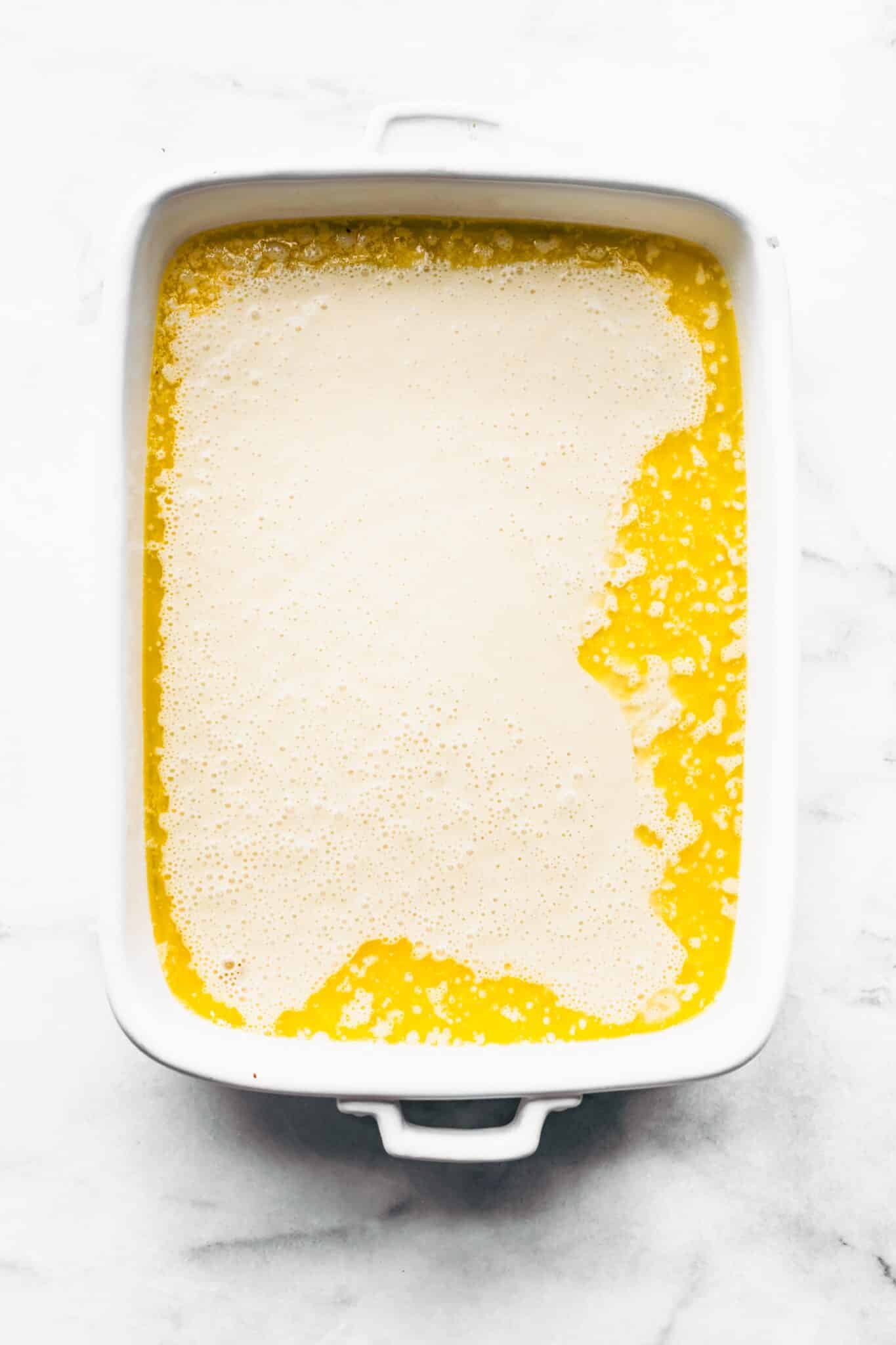 A white baking pan with melted butter and gluten free Swedish pancake batter.