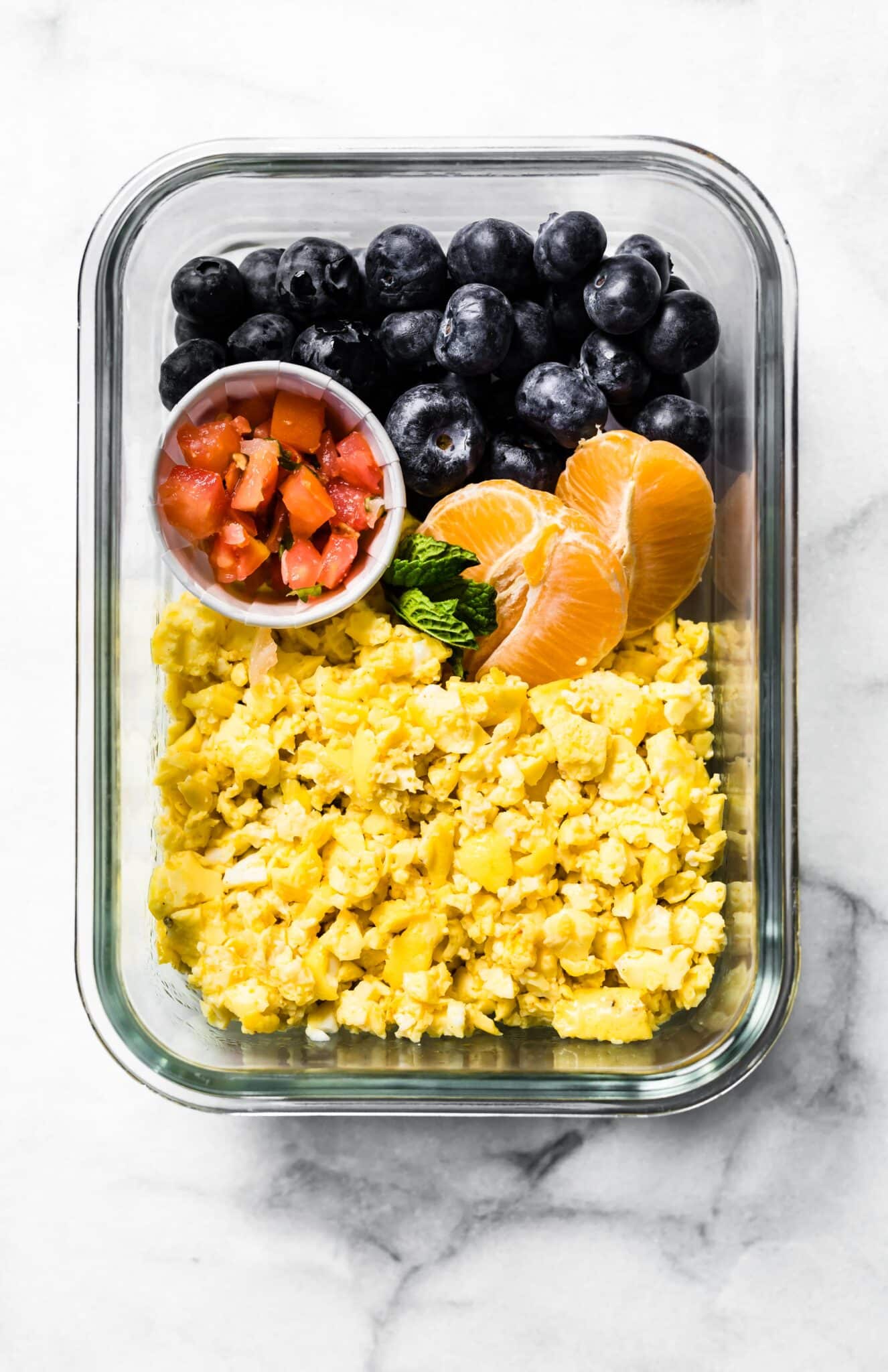 Oven baked scrambled eggs in a meal prep container with oranges, salsa, and blueberries.