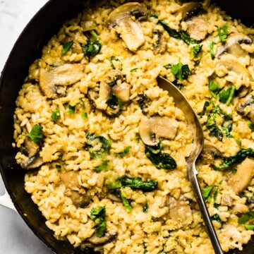 Creamy mushroom risotto in a cast iron pan with spinach and cheese with a spoon.