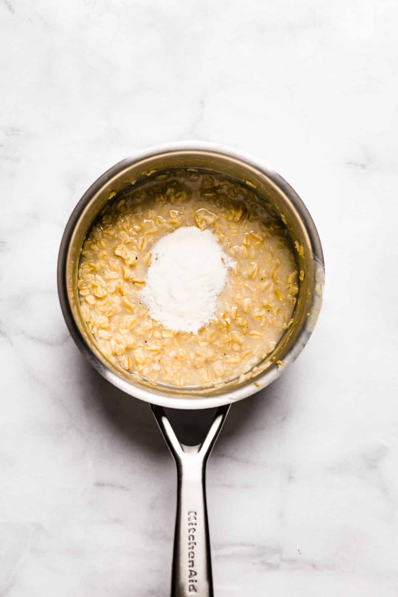 Overhead photo of protein powder on top of cooked oatmeal in a small pot.