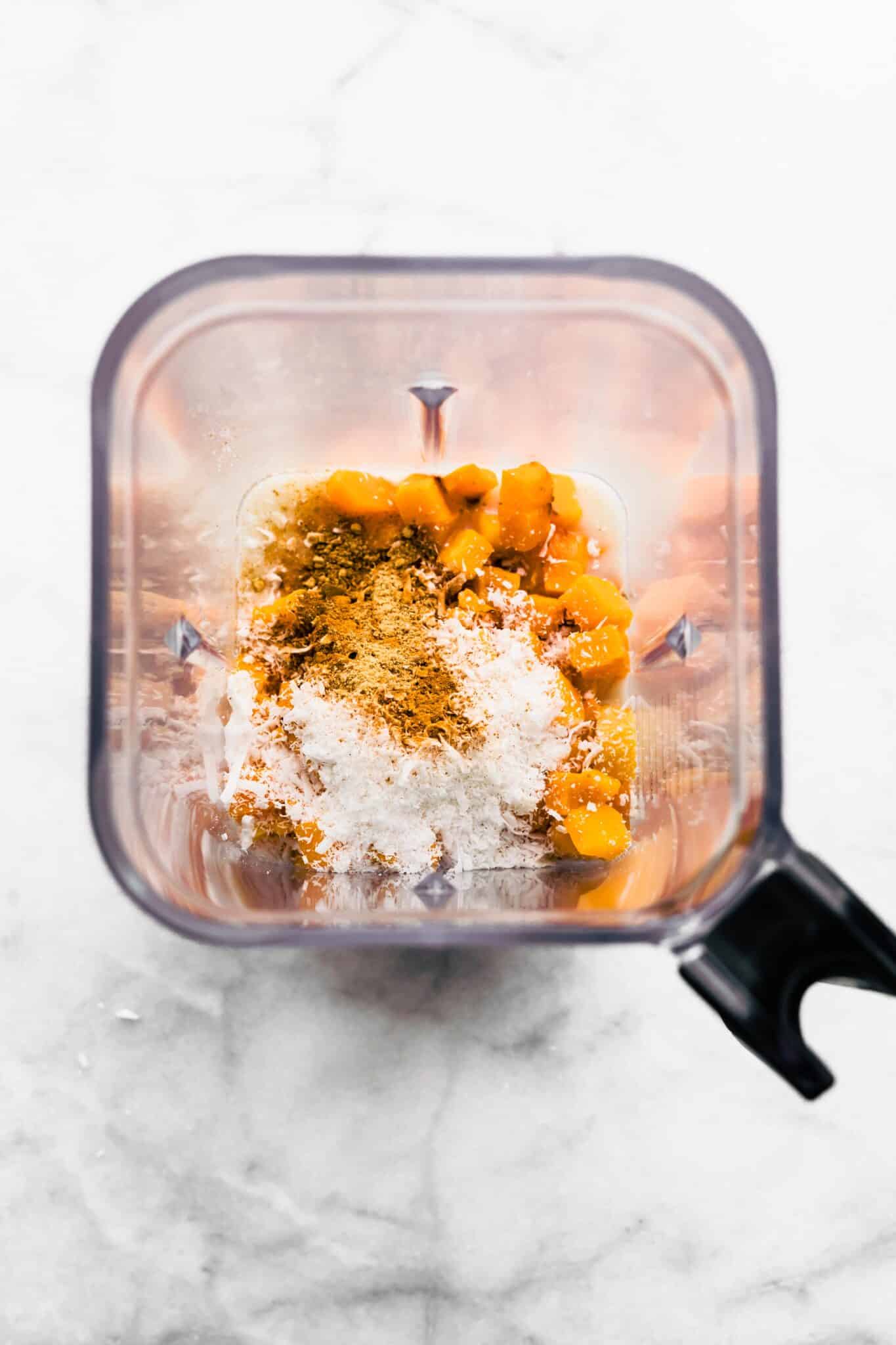 Overhead photo of roasted butternut squash, shredded coconut, and spices in a blender.