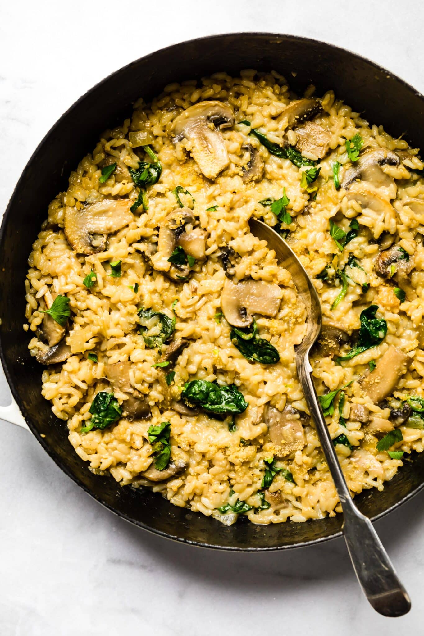 Overhead photo of a spoon digging into a pan of creamy mushroom risotto.