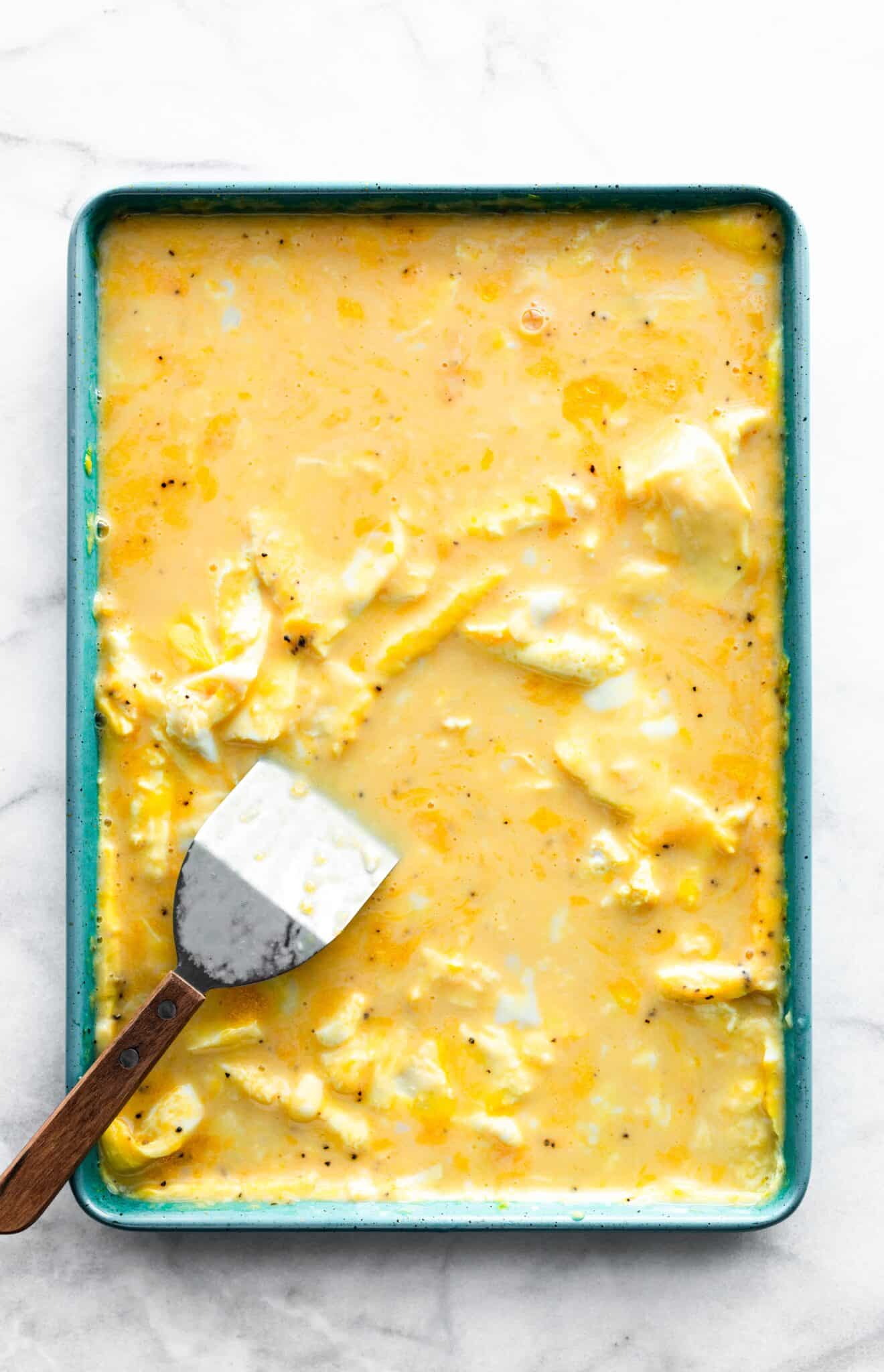 Overhead photo of a spatula in a pan of unbaked scrambled eggs.