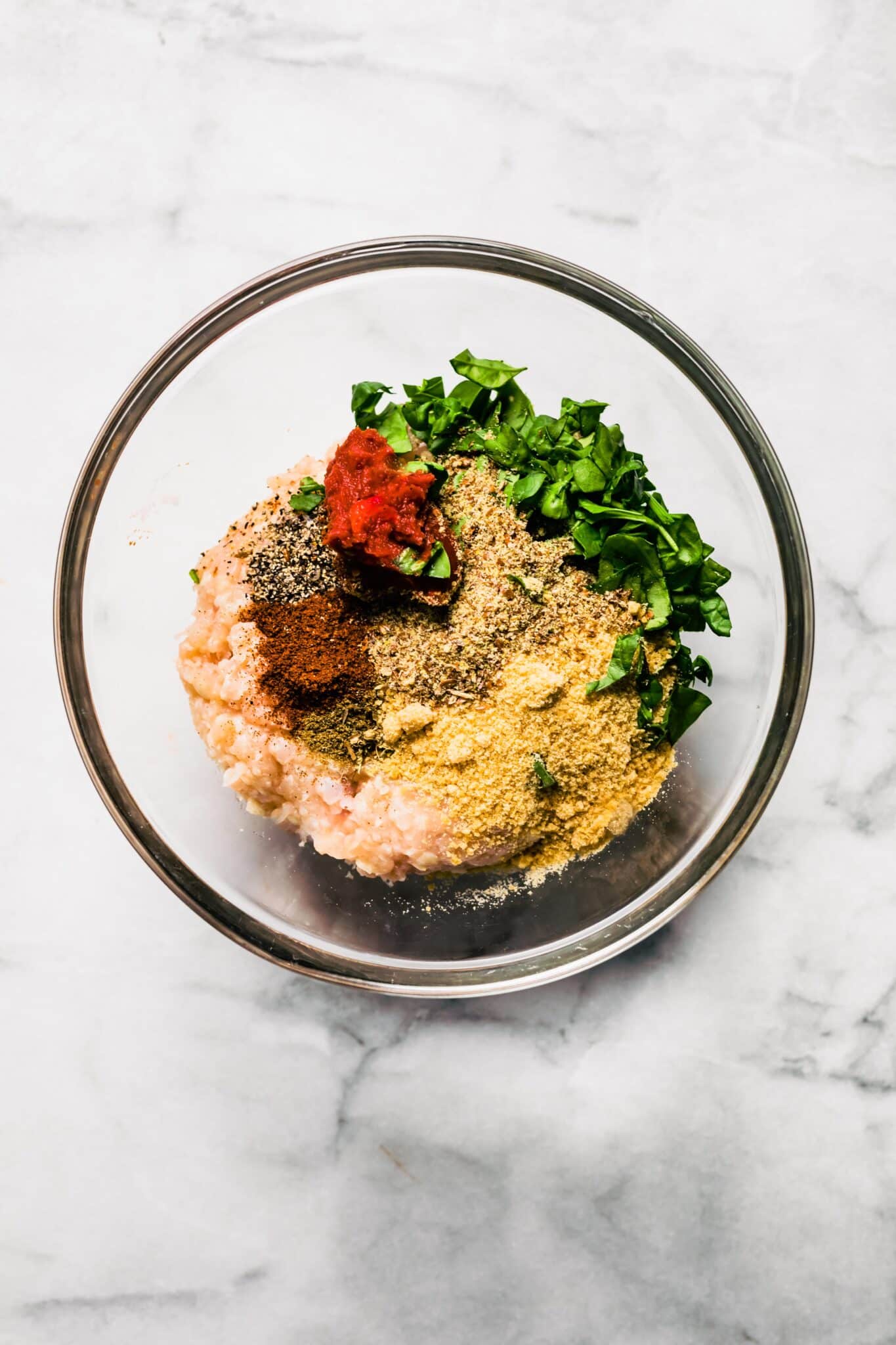 Overhead photo of a glass bowl filled with ground chicken, herbs, and almond flour.