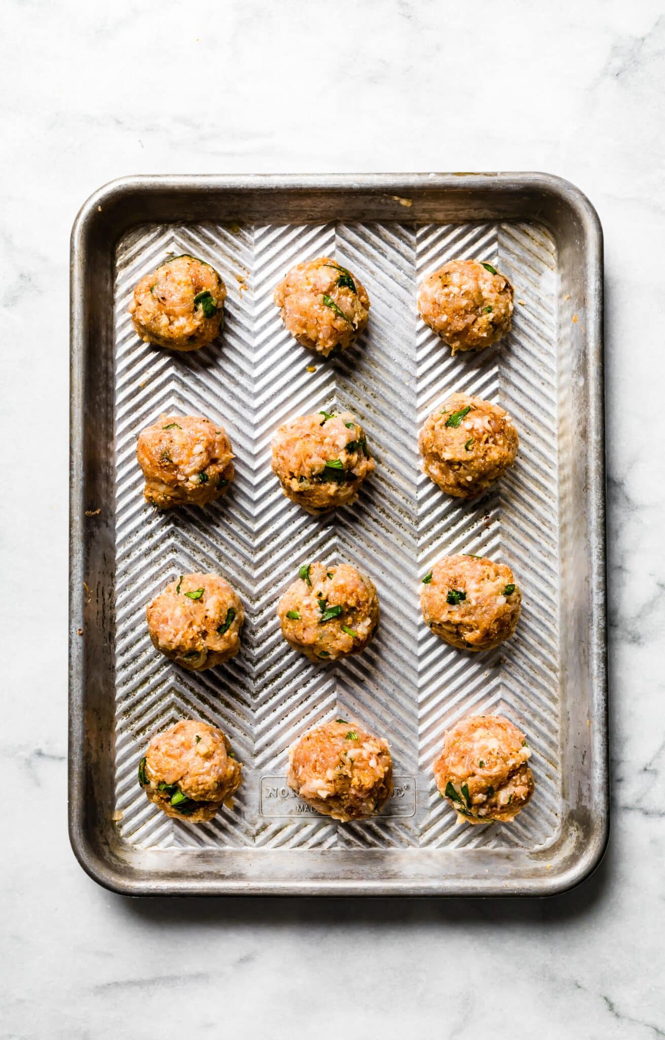 Overhead photo of uncooked chicken meatballs on a baking sheet.