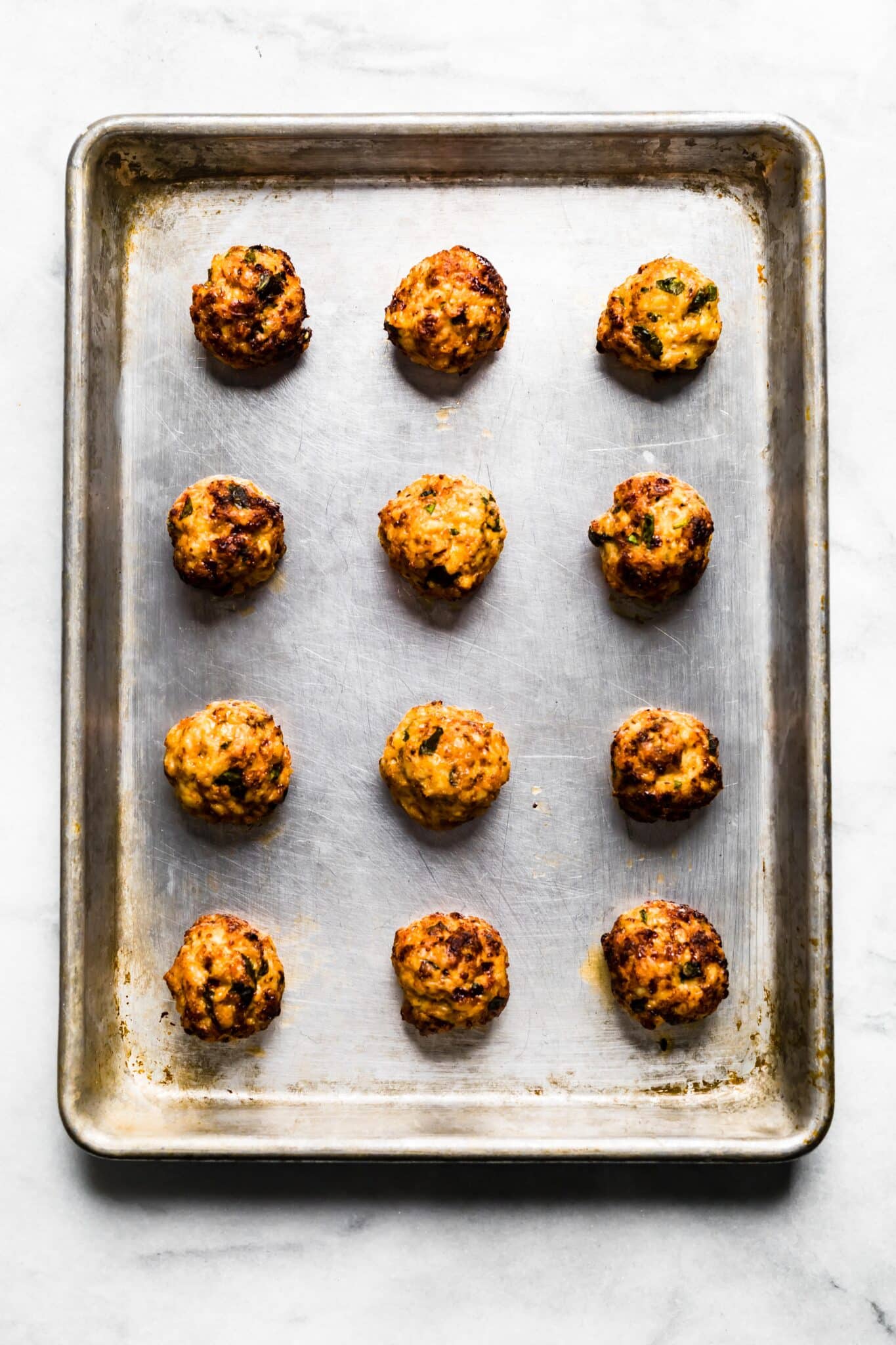 Overhead photo of twelve cooked gluten free chicken meatballs on a sheet pan.