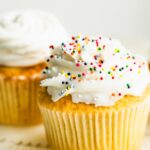 A gluten free vanilla cupcake with white frosting and rainbow sprinkles.