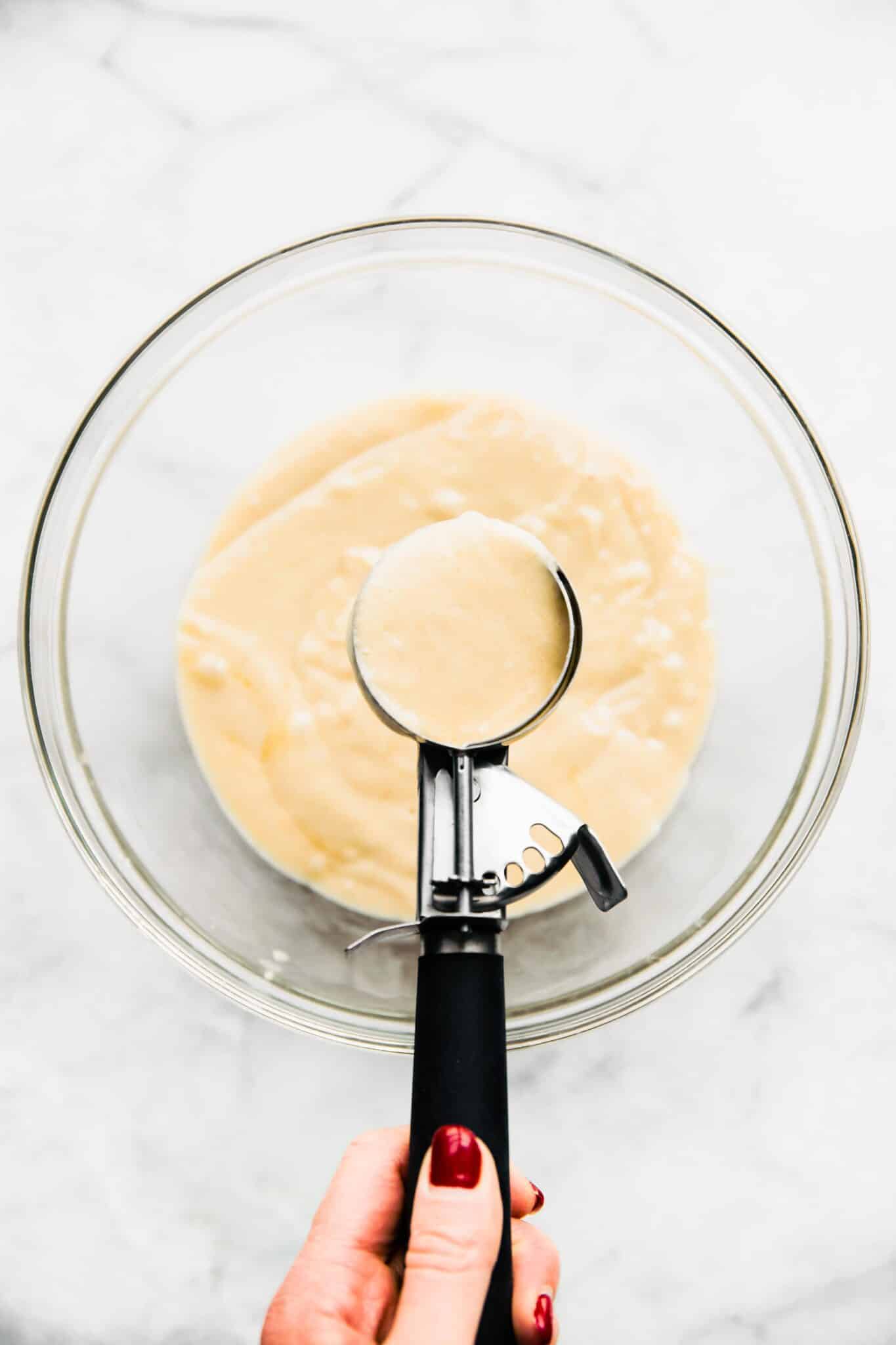 Overhead photo of a woman holding a cookie scoop of vanilla cupcake batter.
