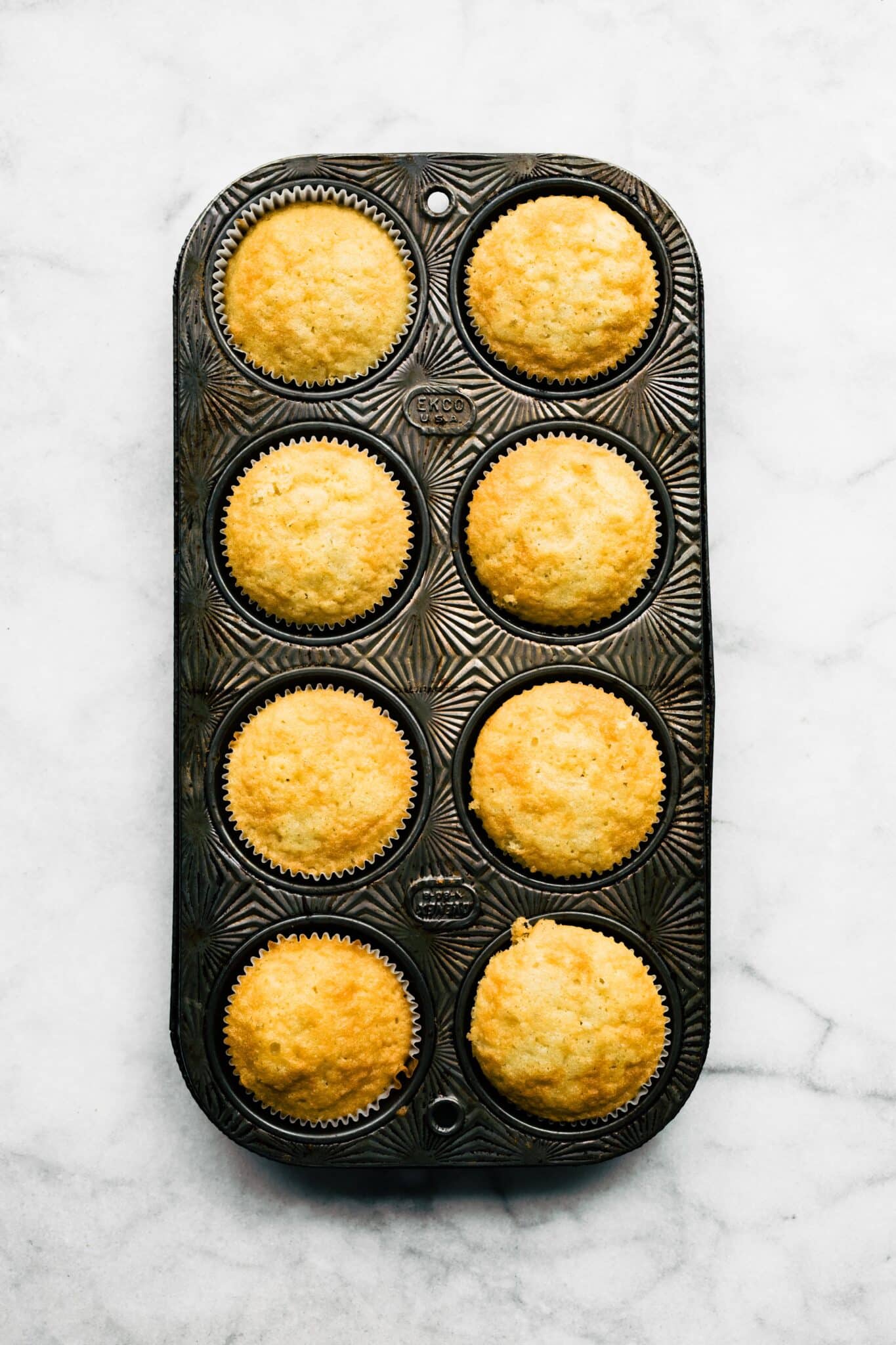 Eight baked gluten free vanilla cupcakes in a vintage muffin pan.