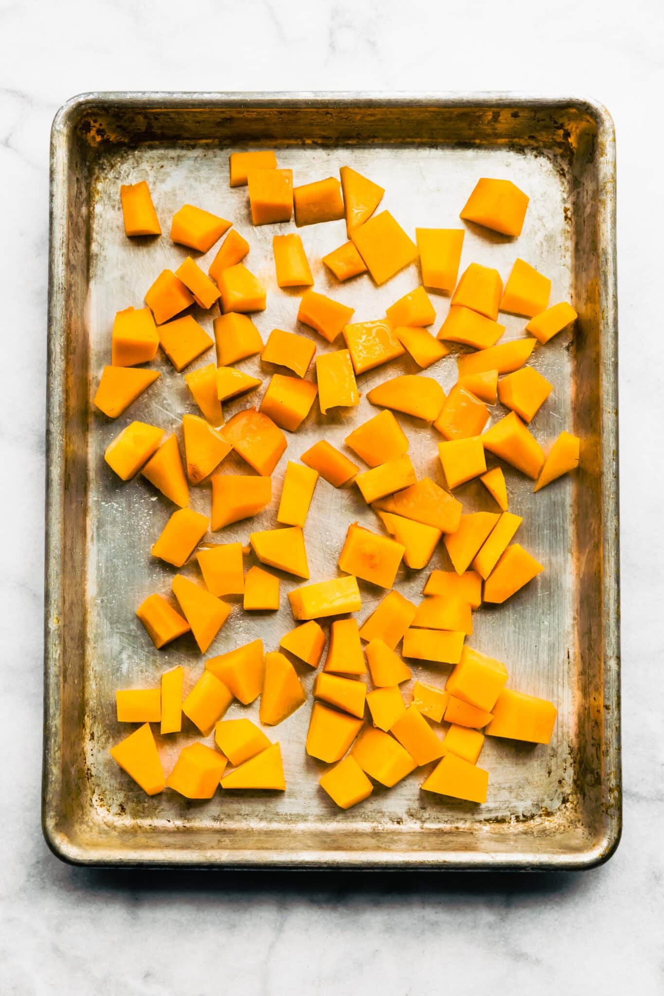 Overhead photo of raw cubed butternut squash on a sheet pan.