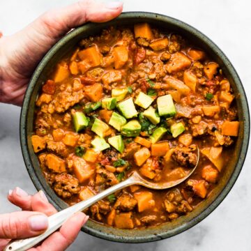 A woman's hands holding a bowl of chipotle sweet potato chili and a spoon.