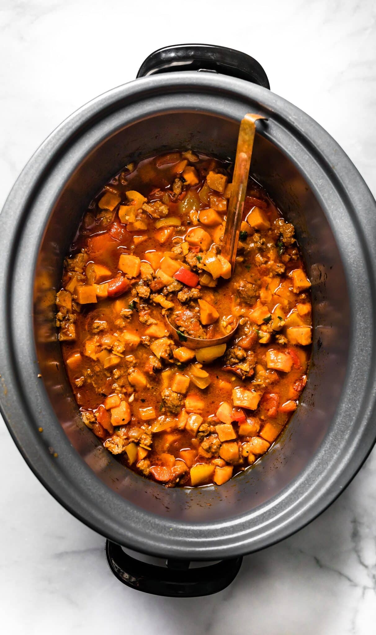 Chipotle Sweet Potato Chili in an oval black crockpot with a copper ladle.