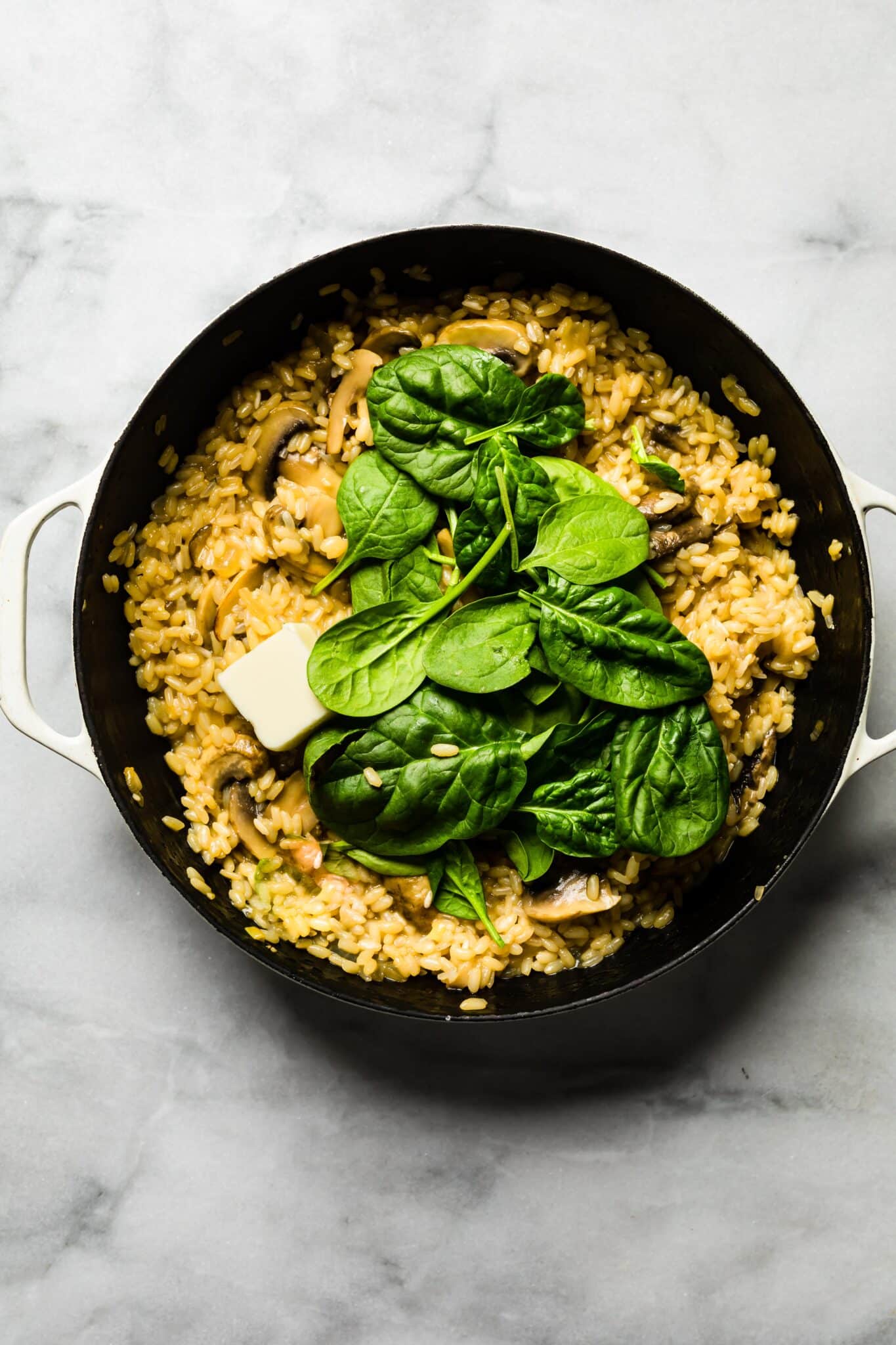 Overhead photo of creamy mushroom risotto with a tab of butter and spinach on top.