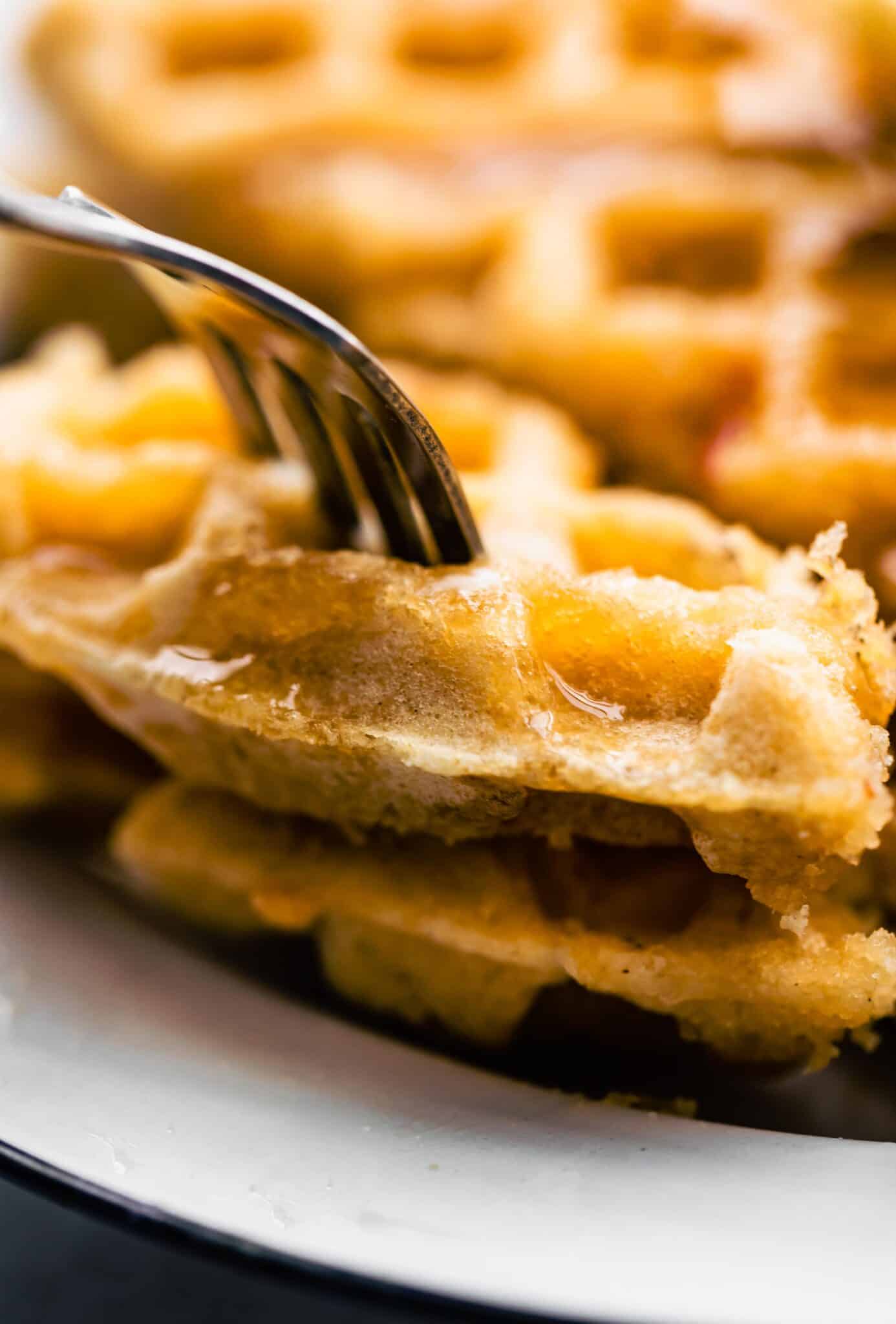 Up close photo of a fork in two pieces of gluten free waffles with syrup.