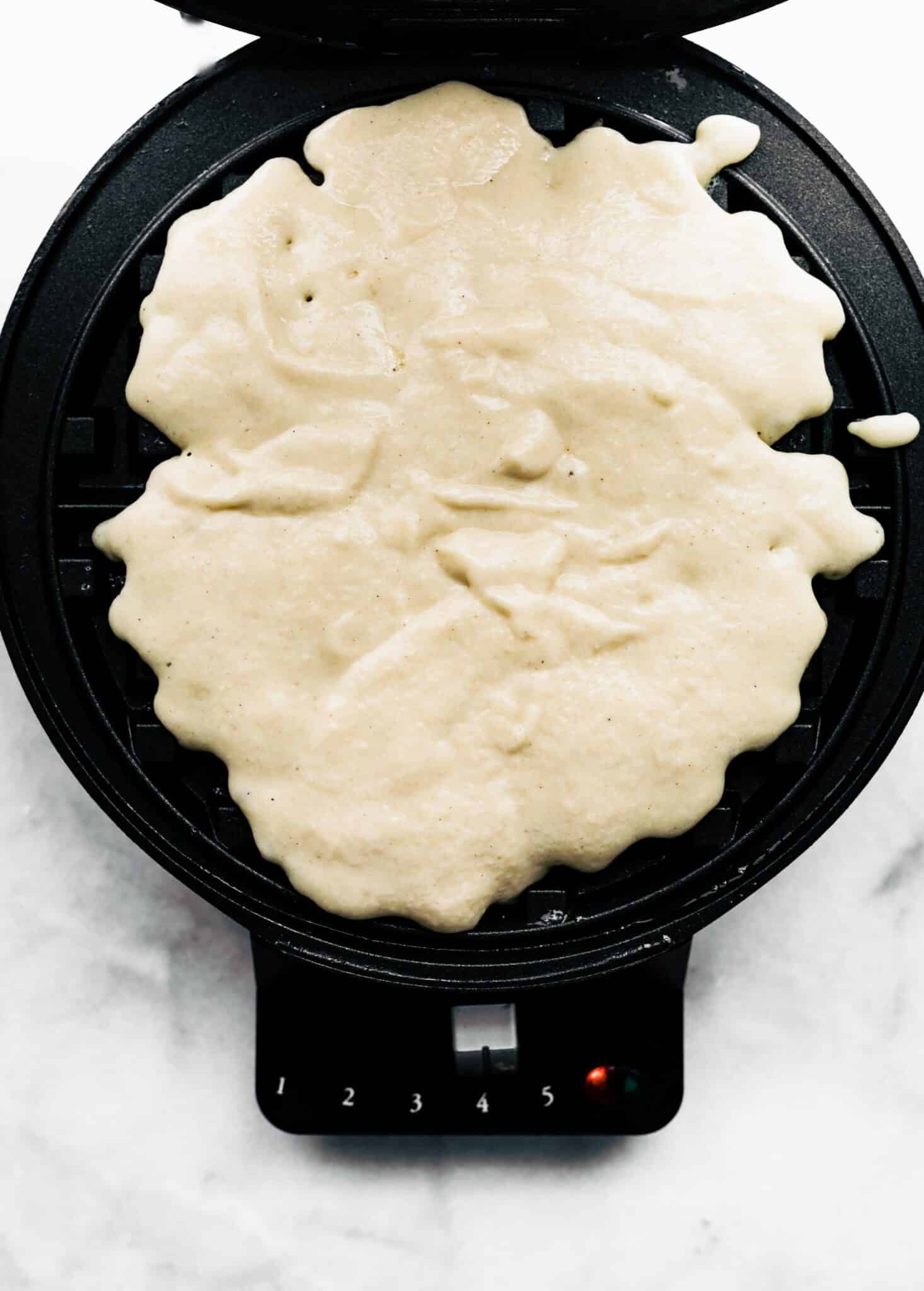 A waffle maker filled with raw gluten free waffle batter.