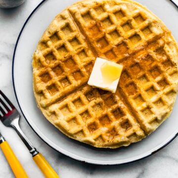 Overhead photo of a gluten free waffle on a plate topped with butter and syrup.