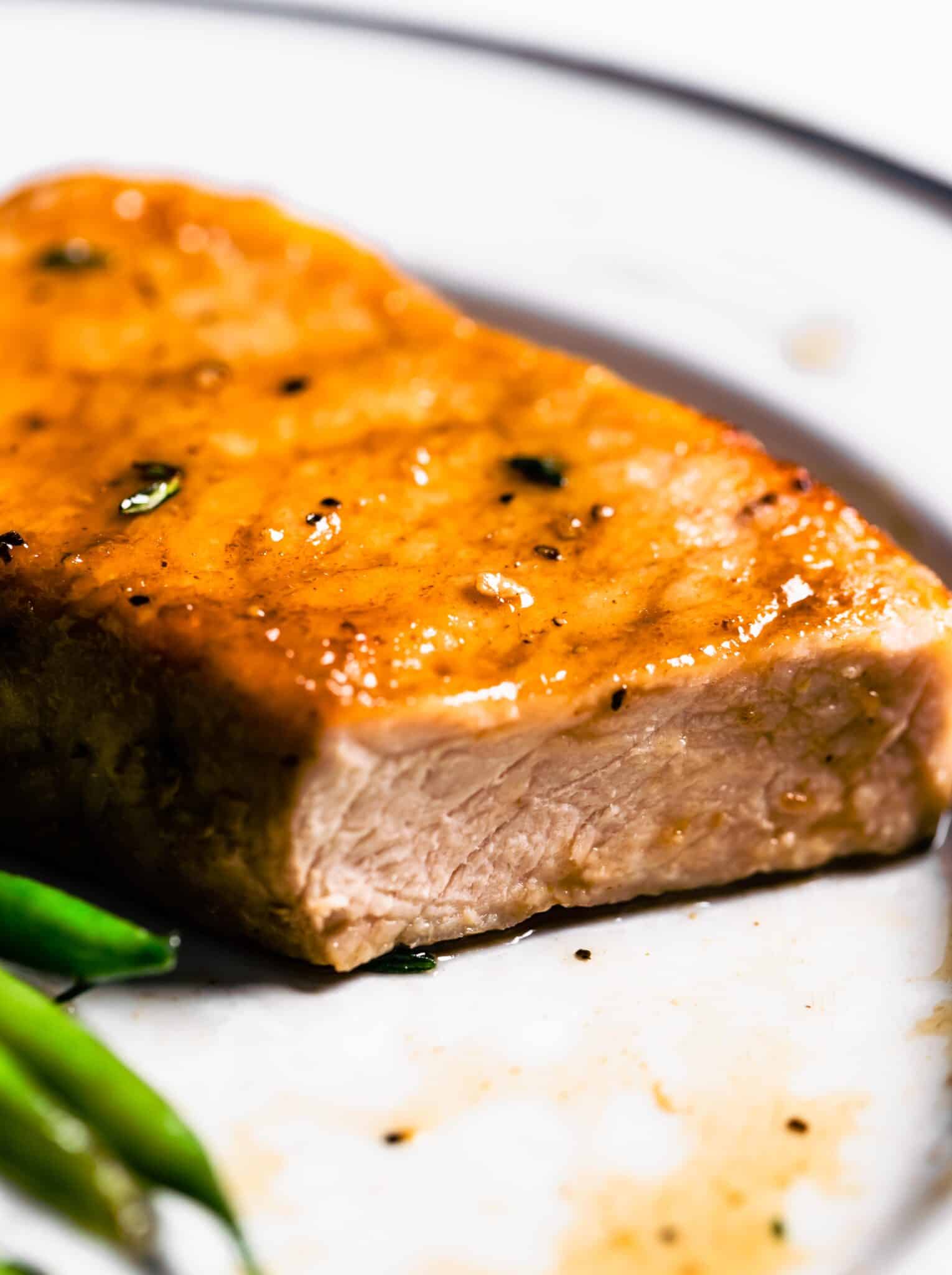 Up close photo of a boneless glazed pork chop on a white plate.