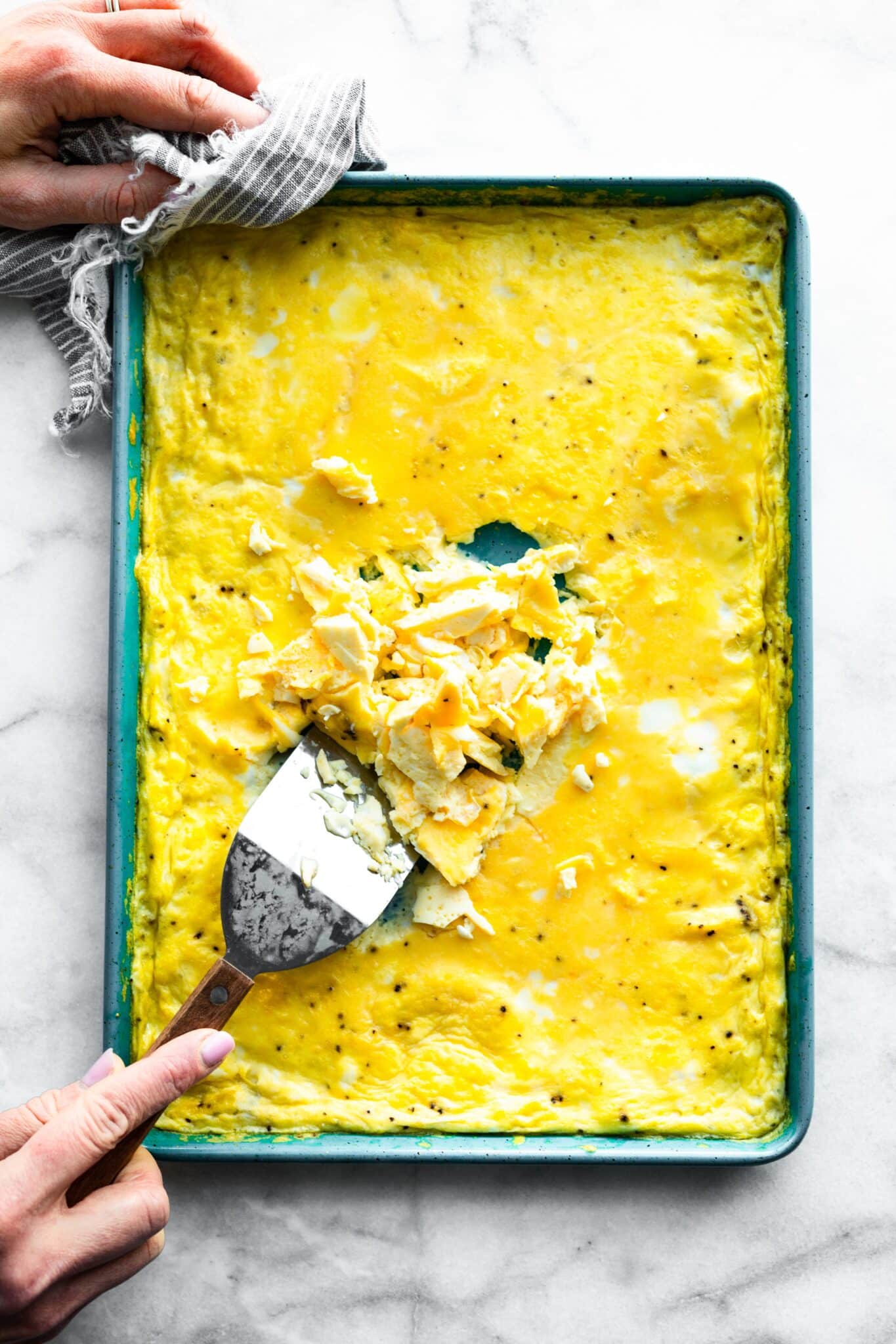 Overhead photo of oven baked scrambled eggs and a woman's hands with a spatula.