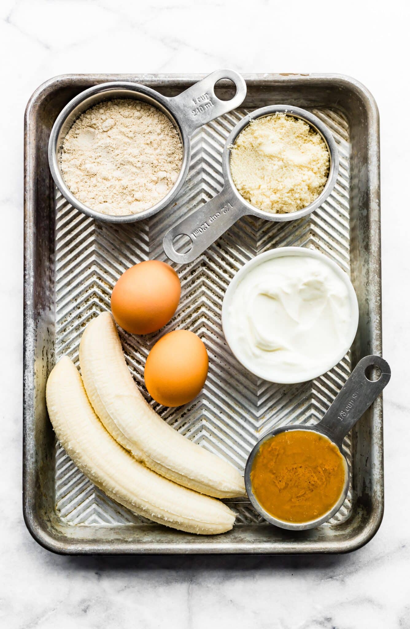 Two bananas, almond flour, eggs and nut butter on a baking sheet.