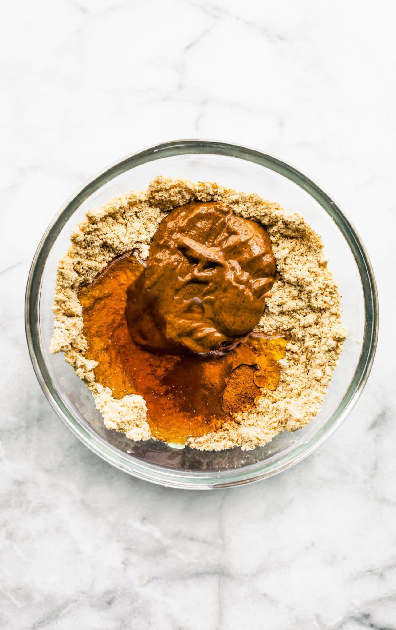 Protein powder, almond butter, and maple syrup in a glass bowl.