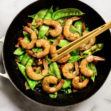 Overhead view wok-fired orange garlic shrimp with stir fry vegetables in white pan
