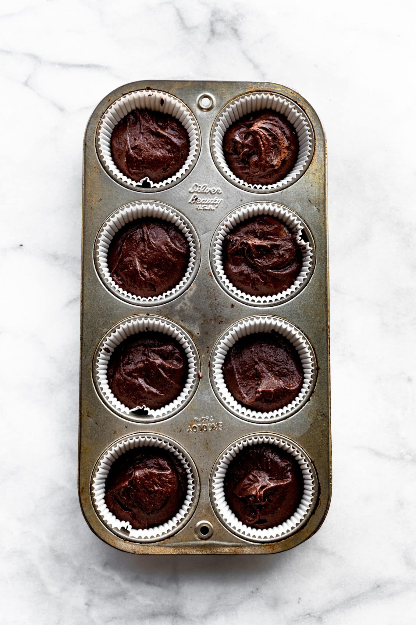 Overhead photo of an eight count muffin pan filled with vegan chocolate cupcake batter.