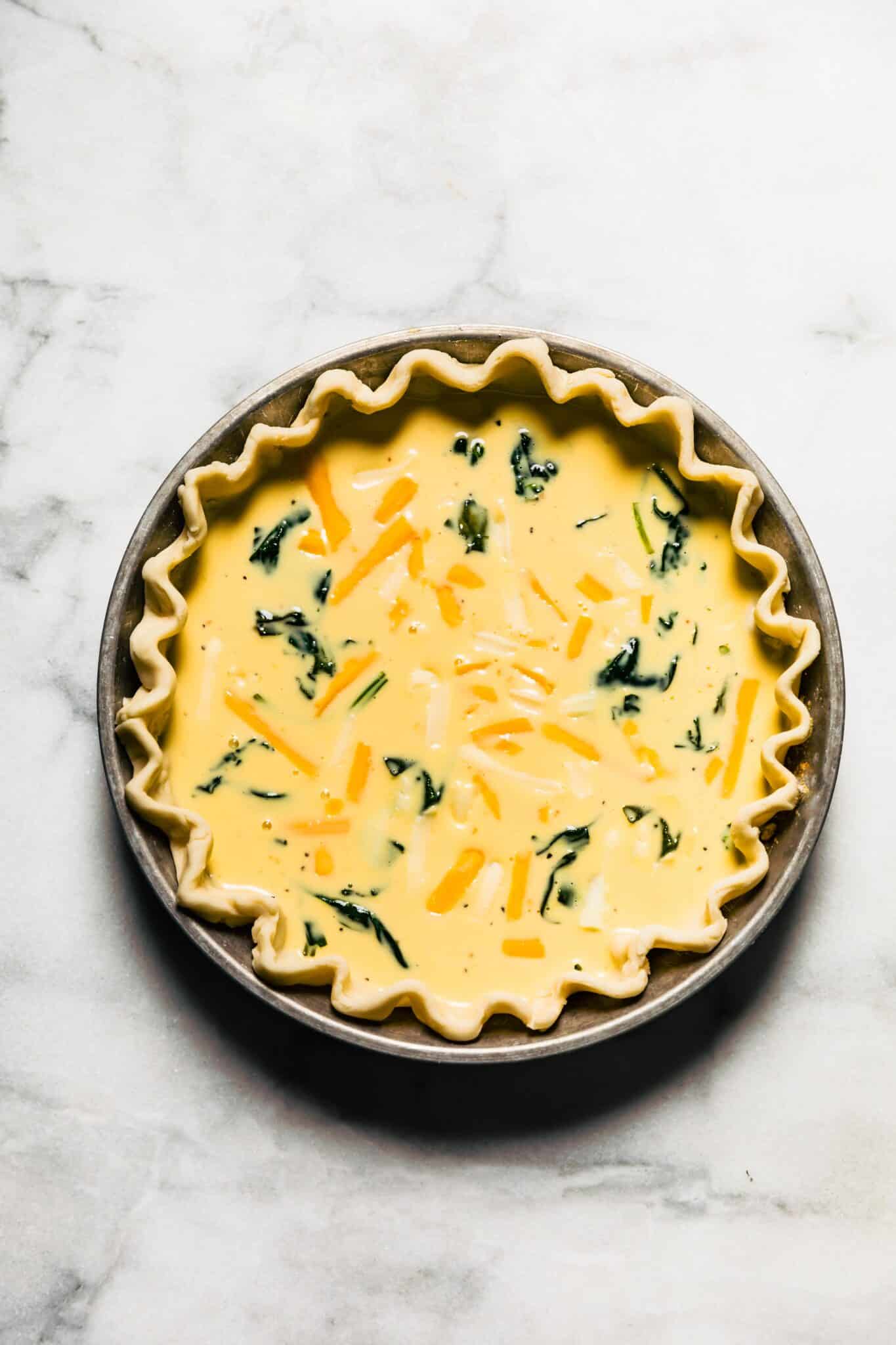 Egg batter with shredded cheese and spinach in a parbaked pie crust.