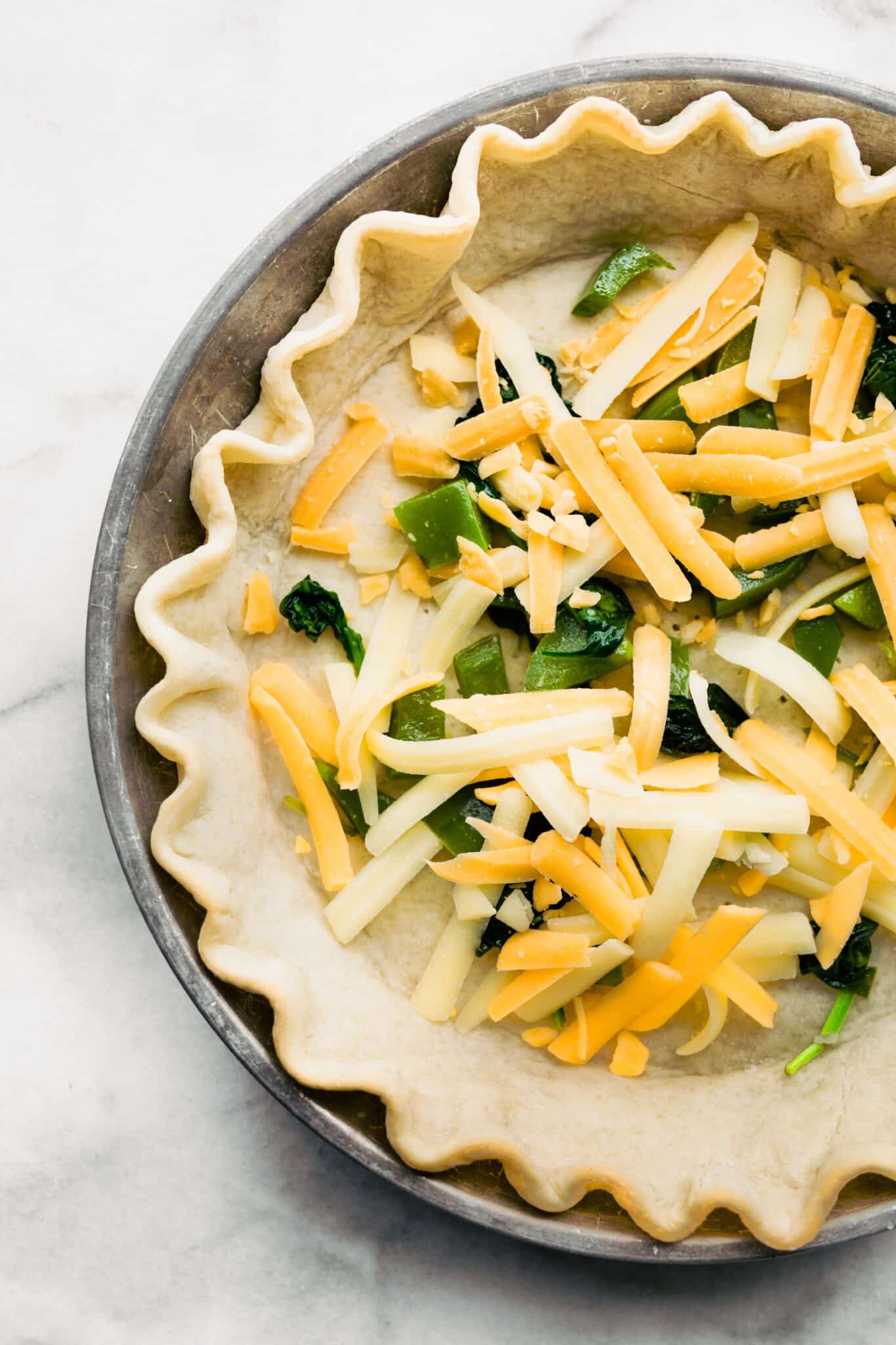 A parbaked pie crust with shredded cheese and vegetables.