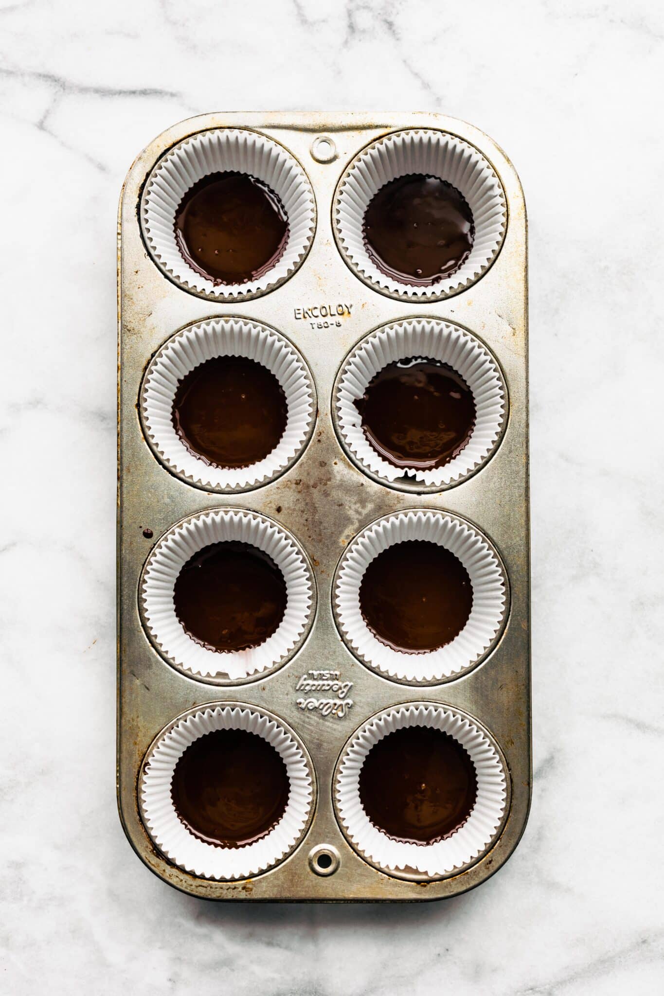 Overhead photo of eight muffin cup liners with melted chocolate in the bottom.