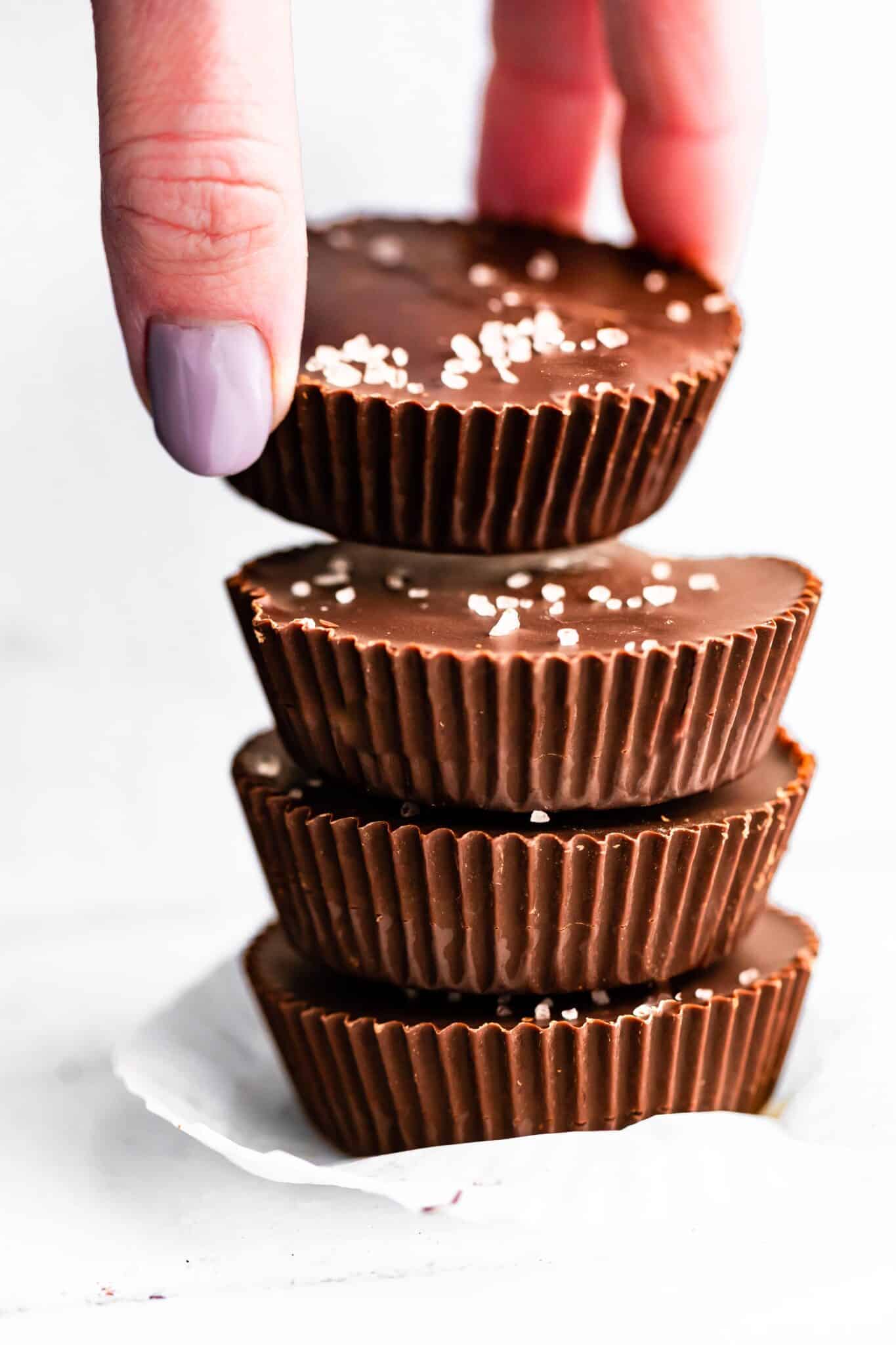 A woman's hands lifting a Chocolate Almond Butter Cup off of a stack of them.