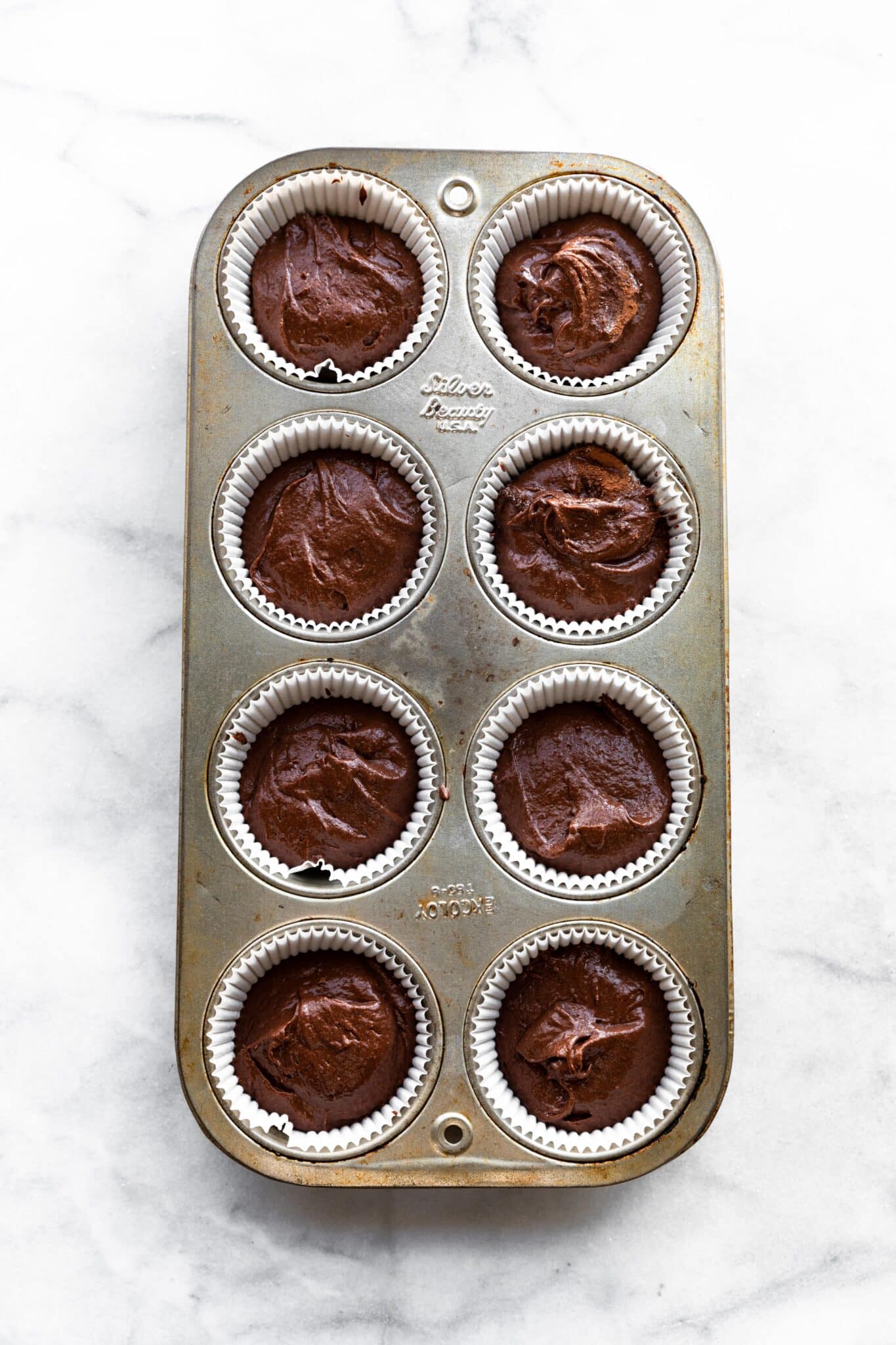 Overhead photo of gluten free chocolate cupcake batter in an eight muffin cup pan.