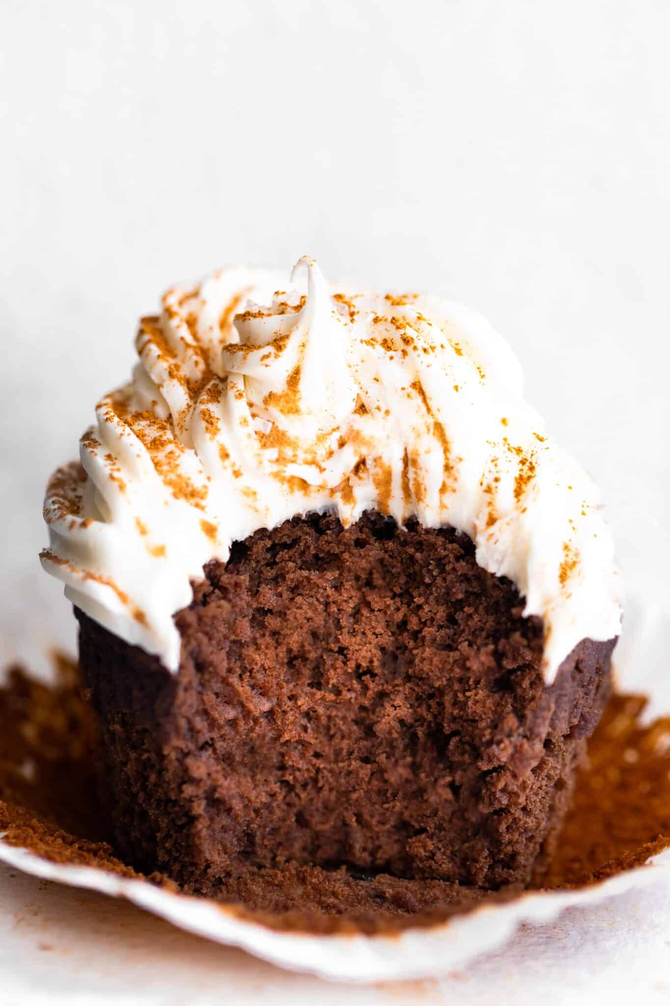 Up close photo of a cupcake topped with vanilla frosting with a bite removed.
