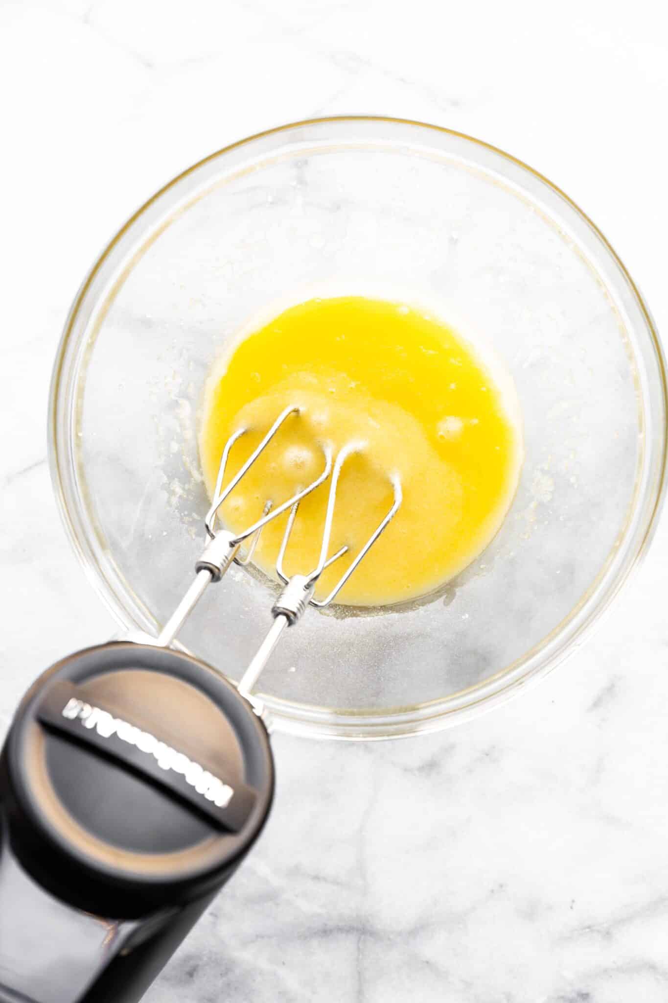 Overhead photo of eggs, sugar, and oil being mixed with a hand mixer.