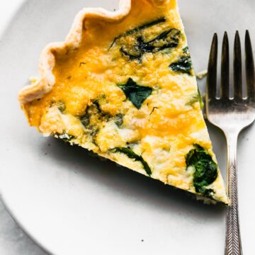 A slice of gluten free quiche on a plate with a fork beside it.