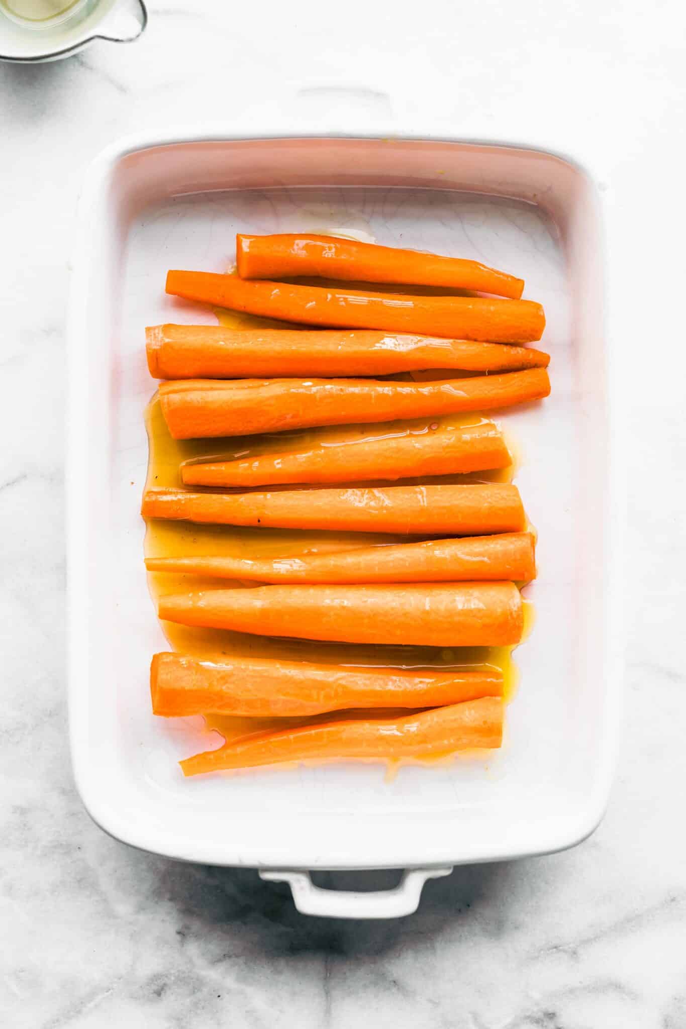 Overhead photo of raw carrots in a maple bourbon glaze in a white baking dish.
