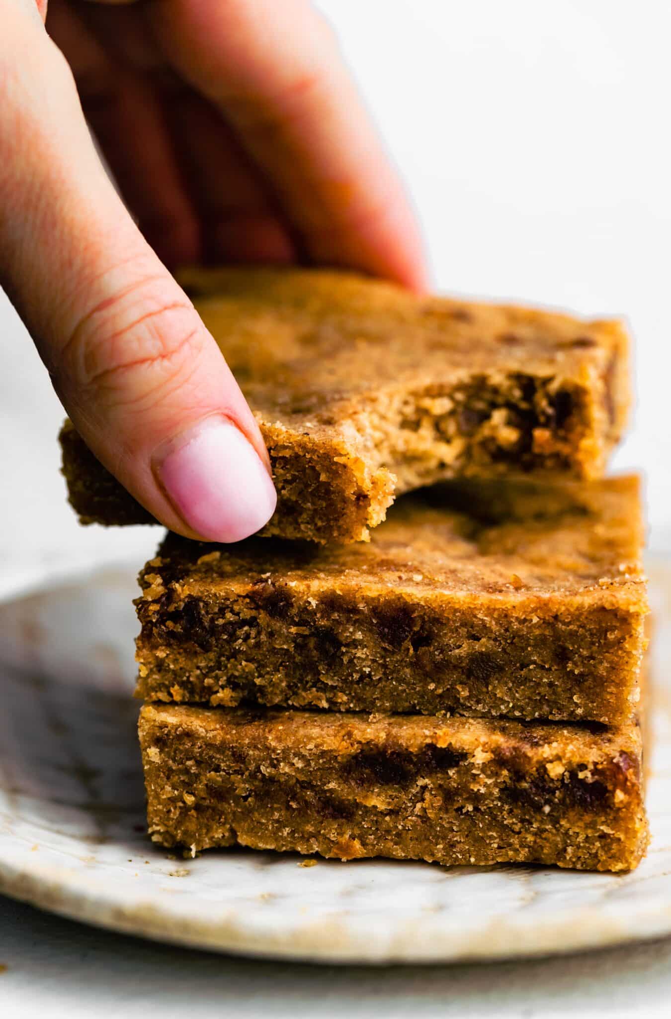 A woman's hand reaching for a stack of soft baked paleo bars on a plate.