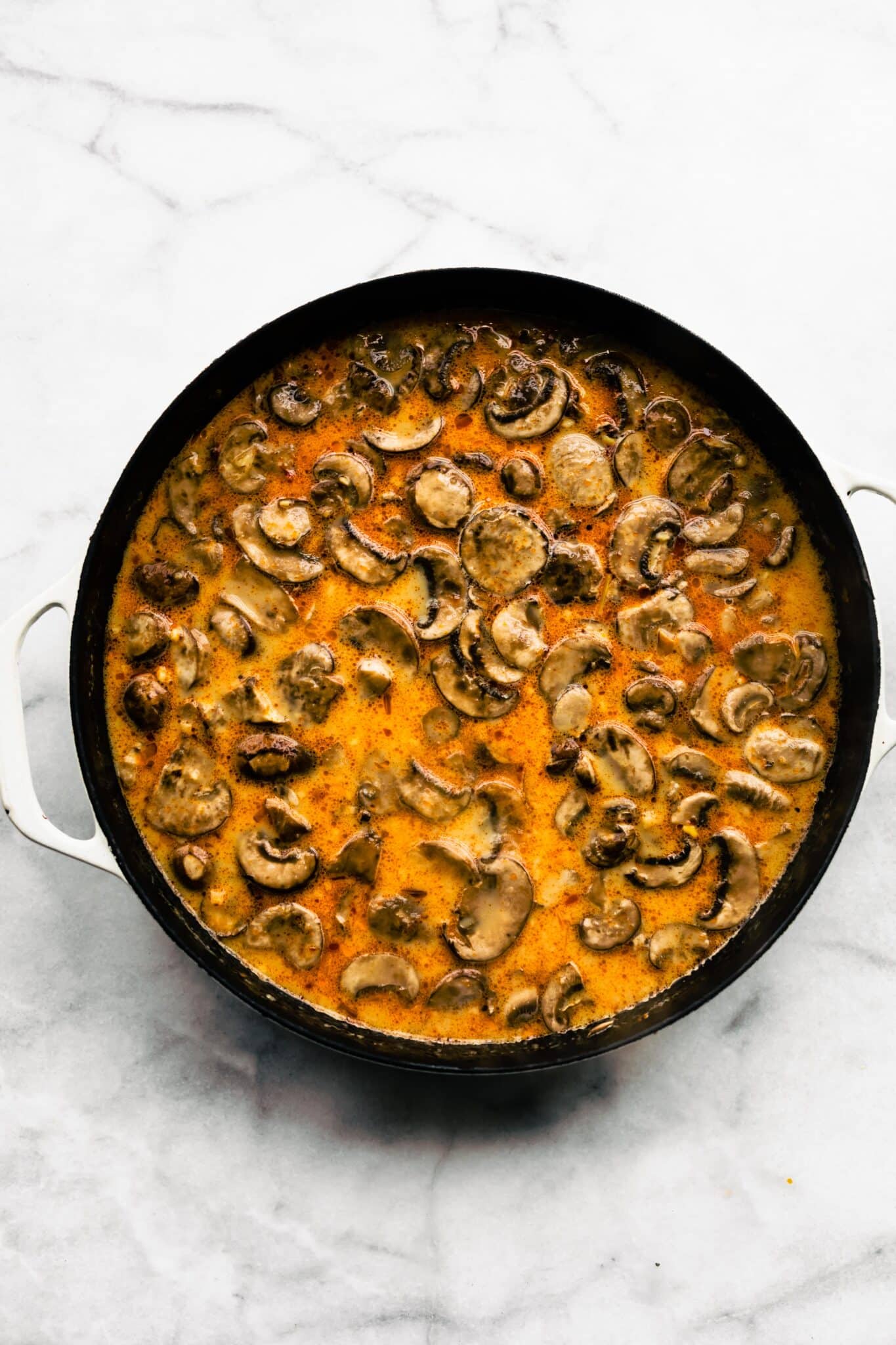 Overhead photo of mushrooms in Thai soup in a black soup pot.