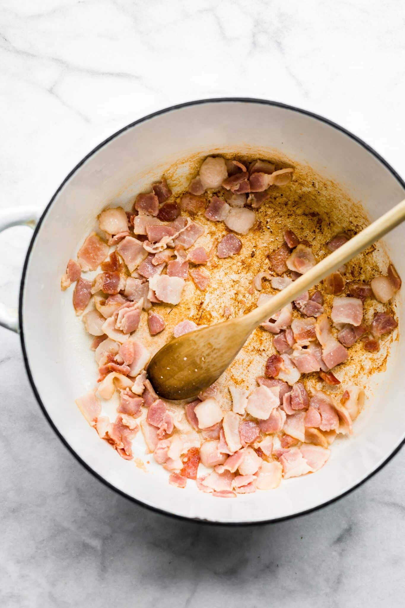 Overhead photo of a wooden spoon in a white pot with diced bacon.