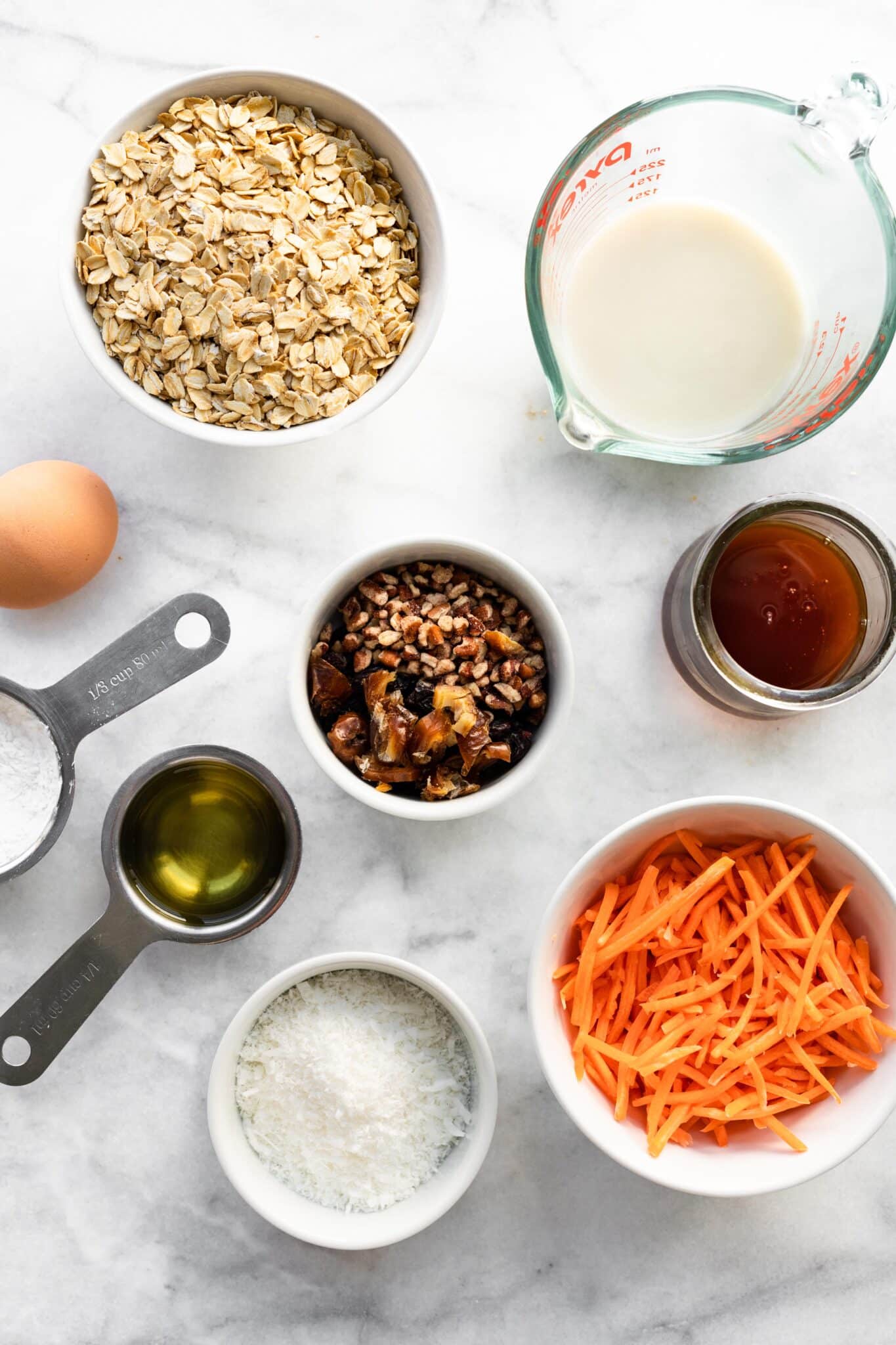 Overhead photo of carrot cake muffin ingredients like oatmeal, shredded carrots and maple syrup.