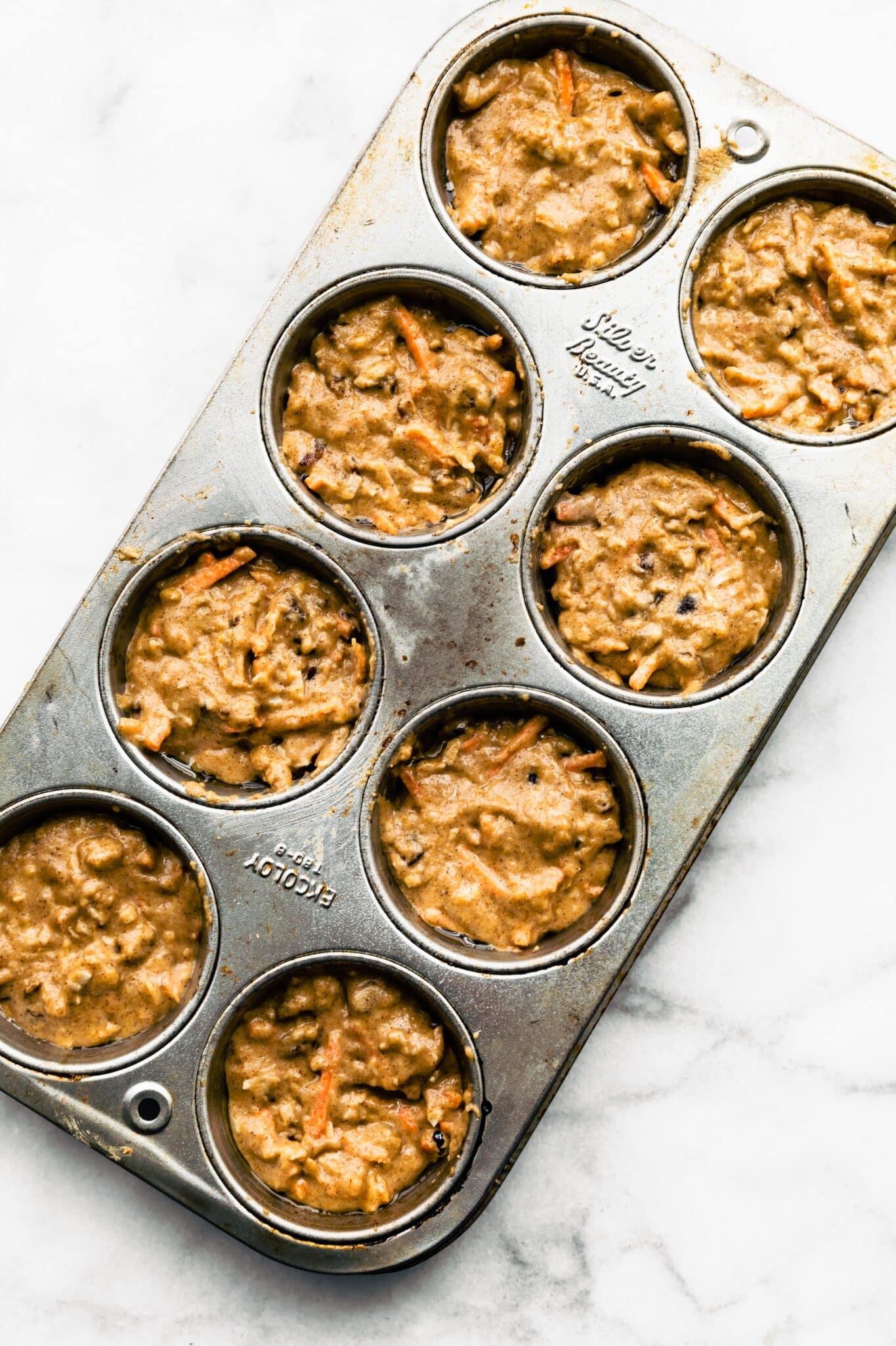 Unbaked healthy carrot cake muffin batter in a muffin pan ready for the oven.