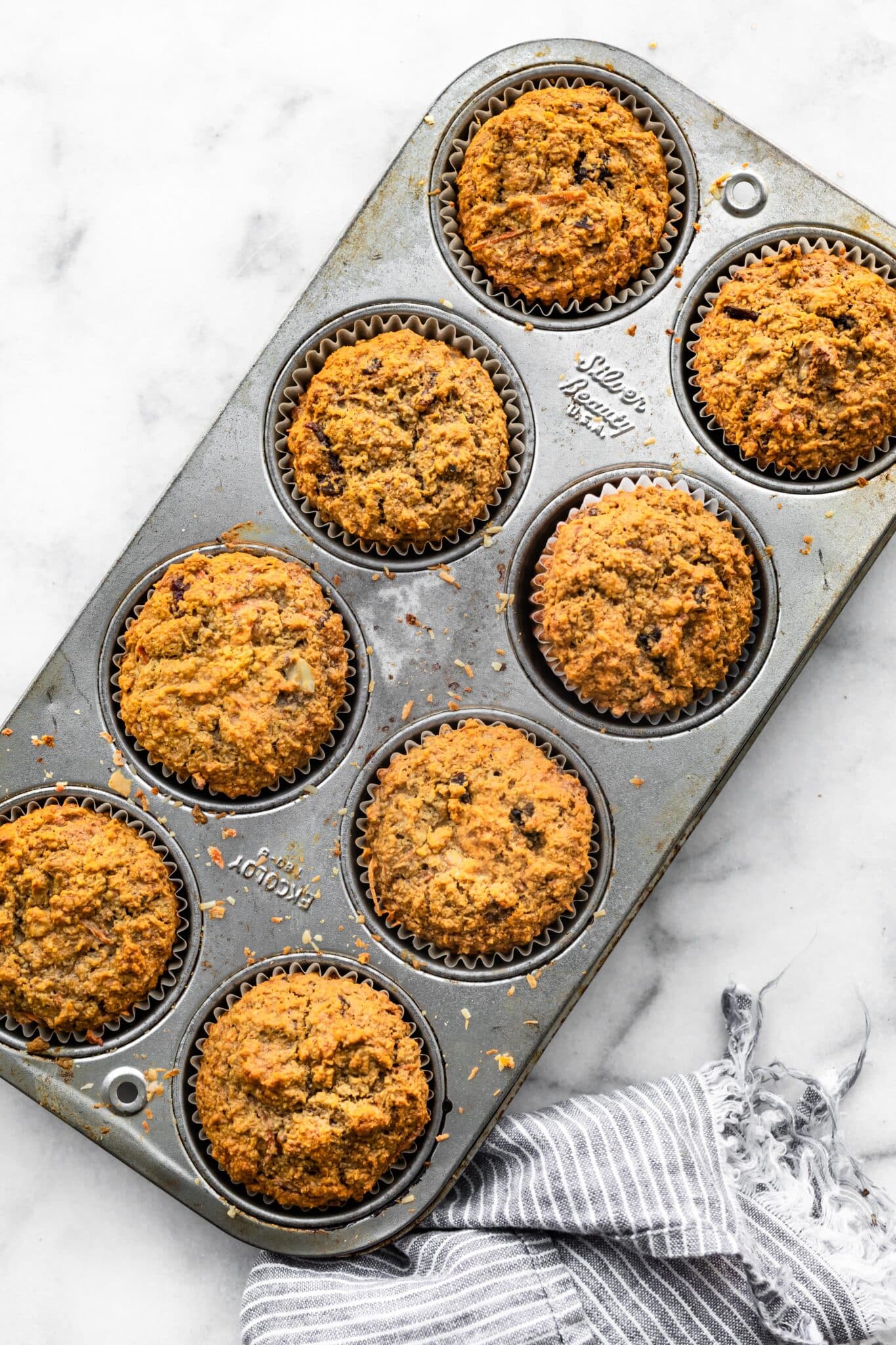 Eight baked gluten free carrot cake muffins in a metal muffin pan.