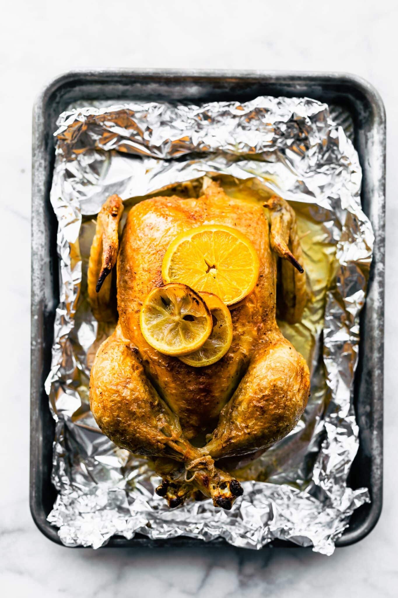 Overhead photo of a baked whole chicken with lemon slices on top.