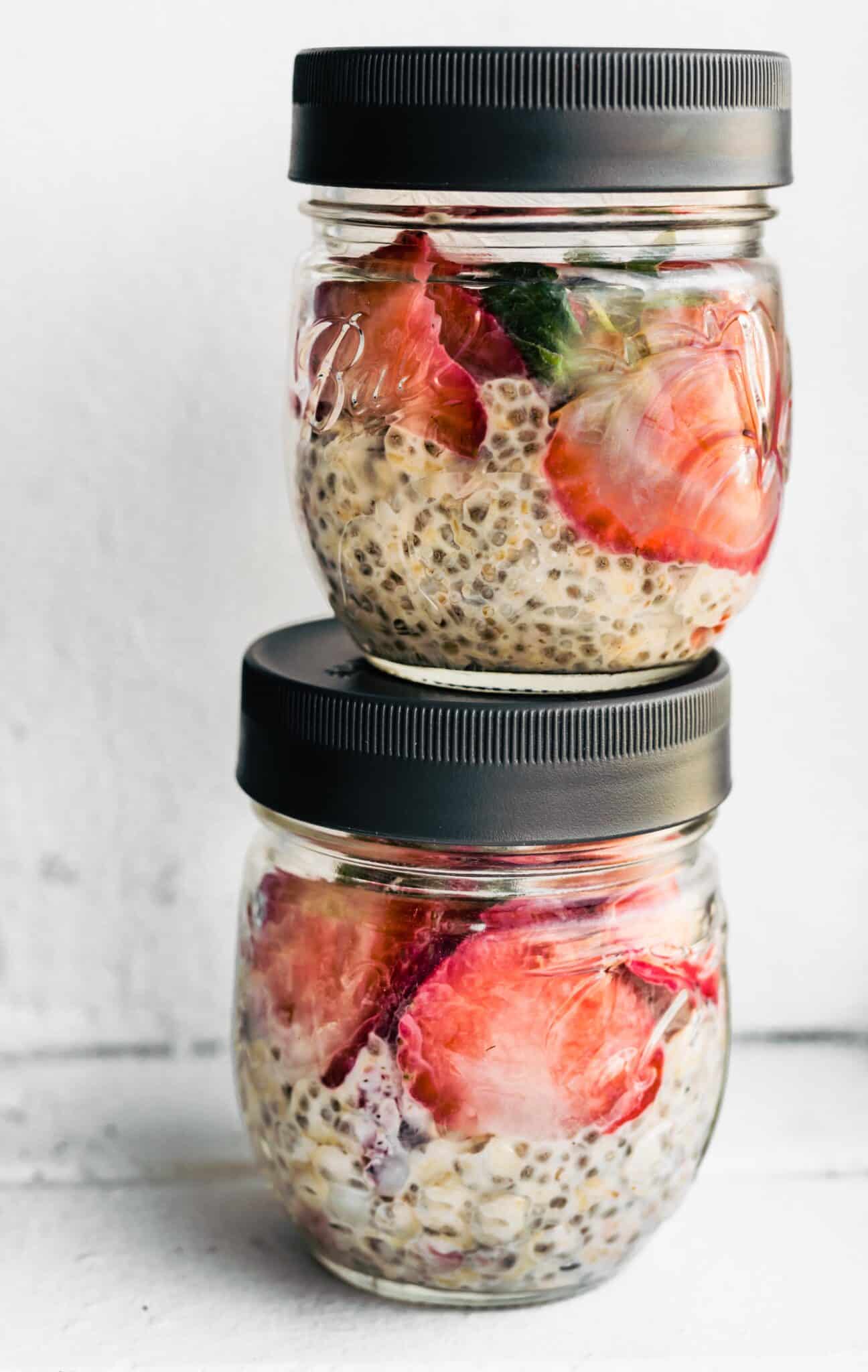 Strawberry overnight oats in two jars with black lids stacked on top of each other.