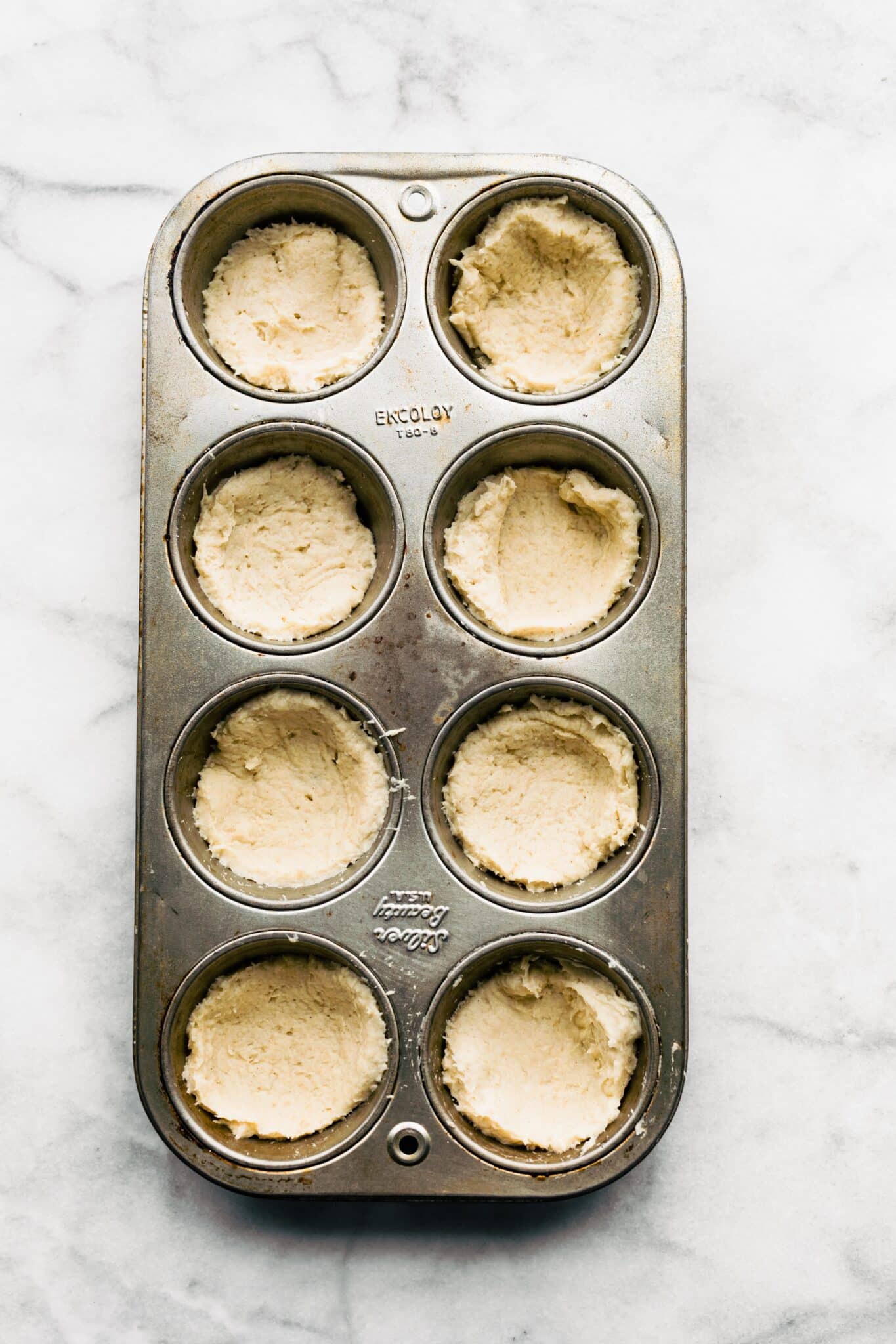 Gluten free pizza dough cut into small rounds placed in 8 muffin tin wells.