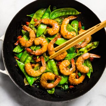 Orange shrimp stir fry in a black pan with chopsticks.