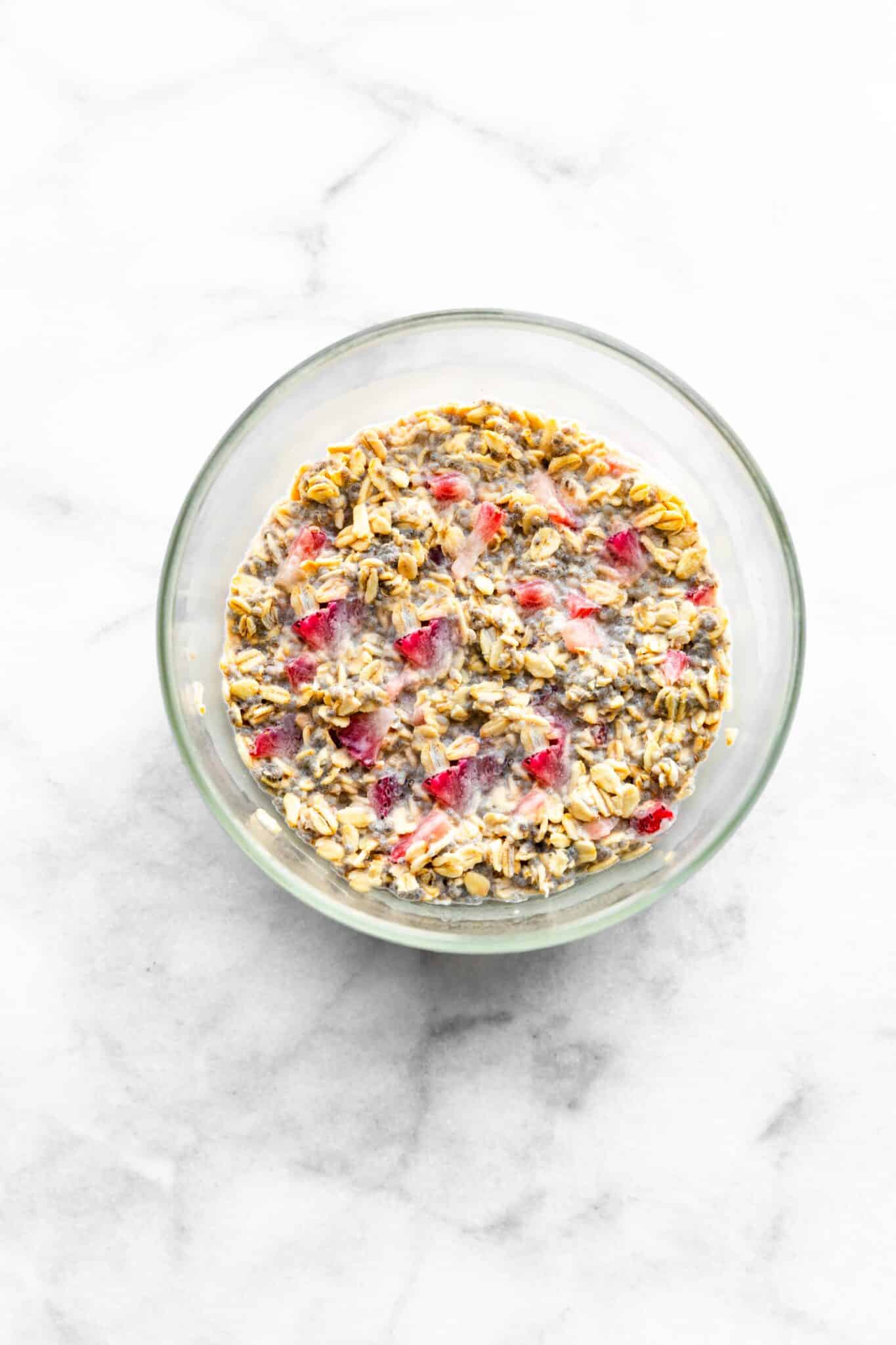 Strawberry overnight oats in a clear glass bowl on a white countertop.
