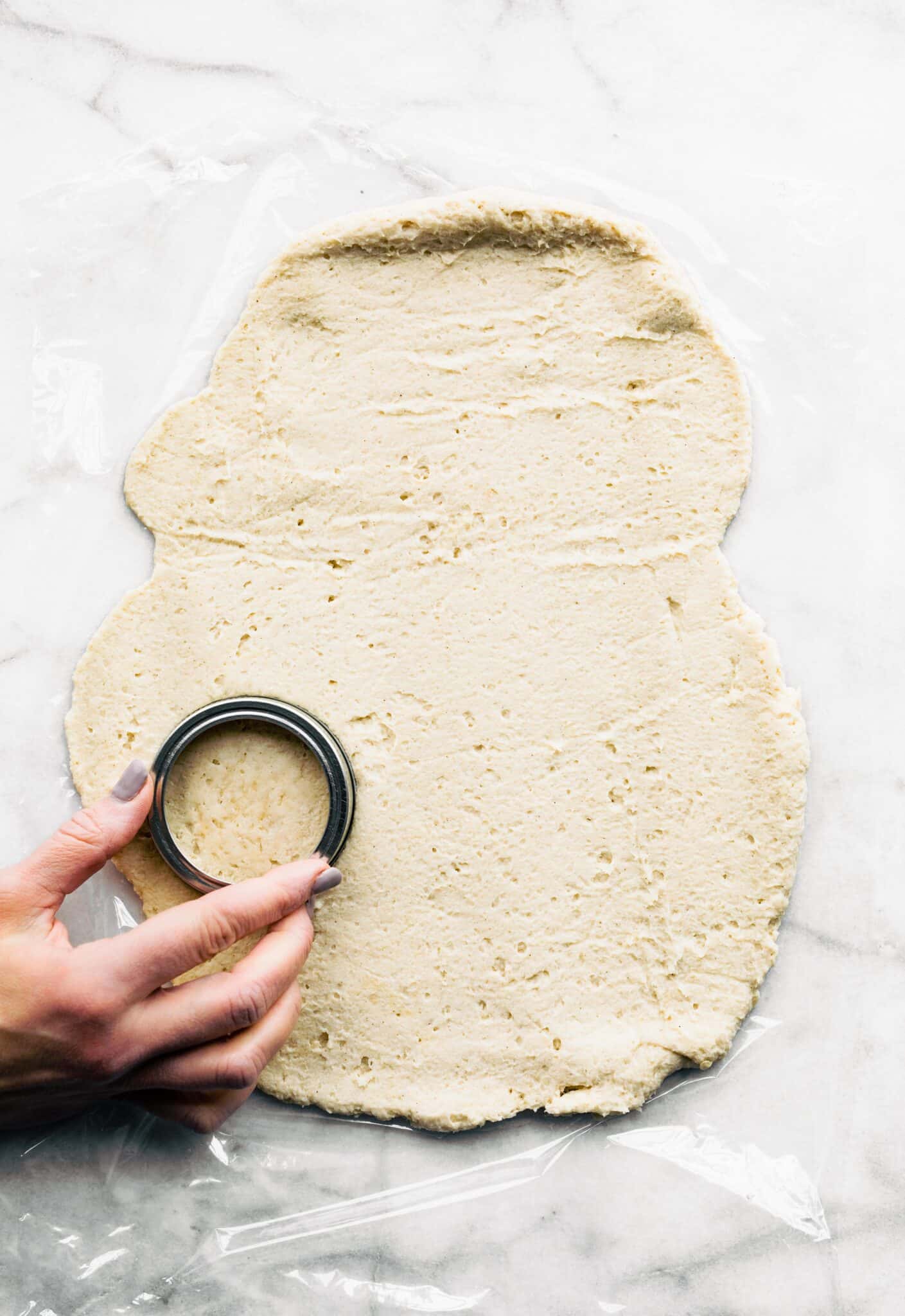 Overhead photo of a woman's hand using a mason jar ring to cut pizza dough.