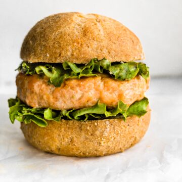A gluten free hamburger bun with a salmon burger and lettuce.