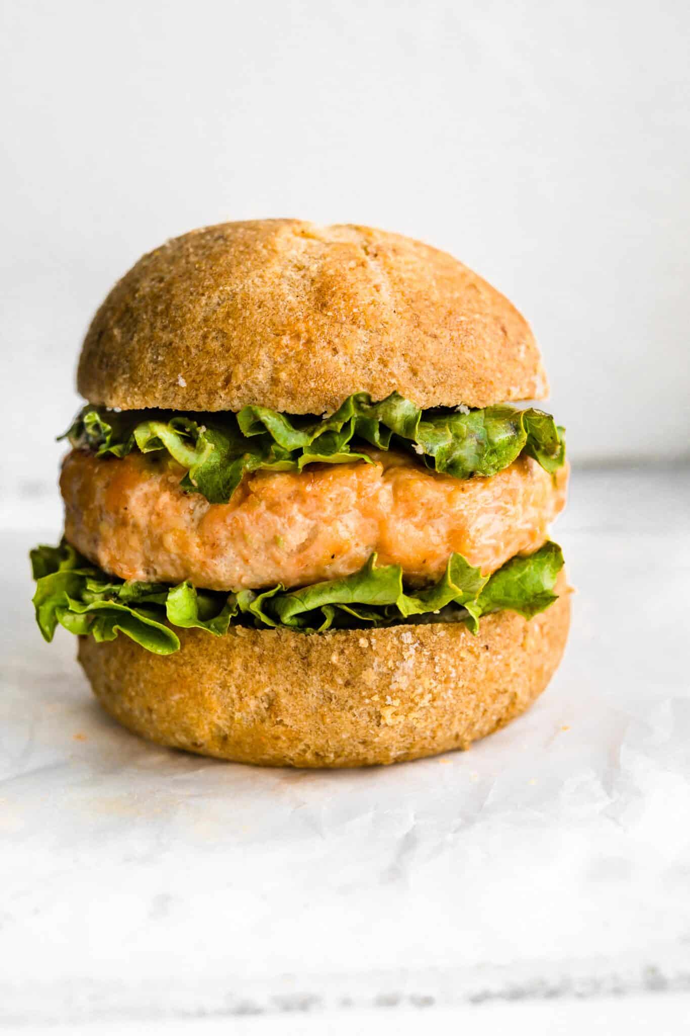 A gluten free hamburger bun with a salmon burger and lettuce.
