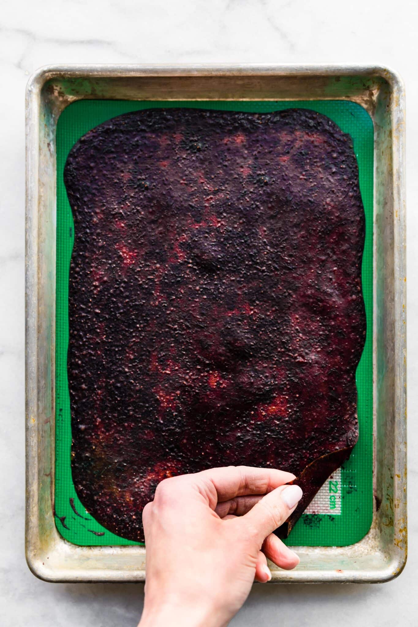 Overhead photo of a woman's hand pulling dried fruit puree from a silpat liner.